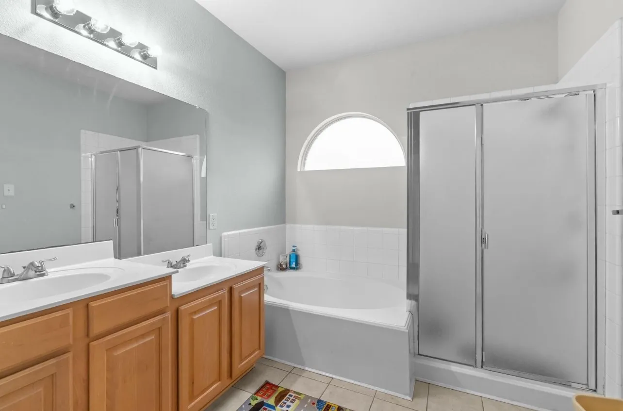 Dual vanity with wood-finish cabinetry, built-in bathtub, and enclosed shower