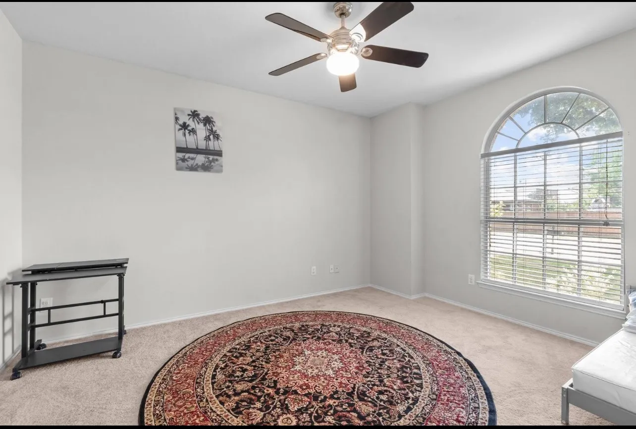 Arch-top window with blinds, ceiling fan with integrated lighting, and neutral carpeting