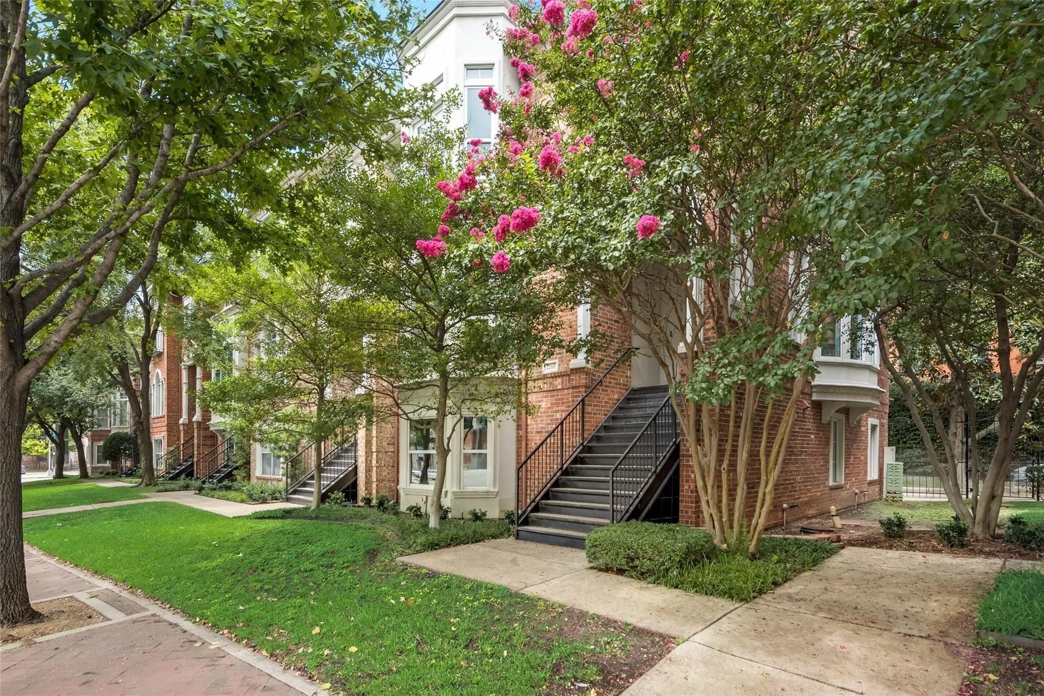Brick exterior with a white trim bay window, black exterior staircase, and mature landscaping