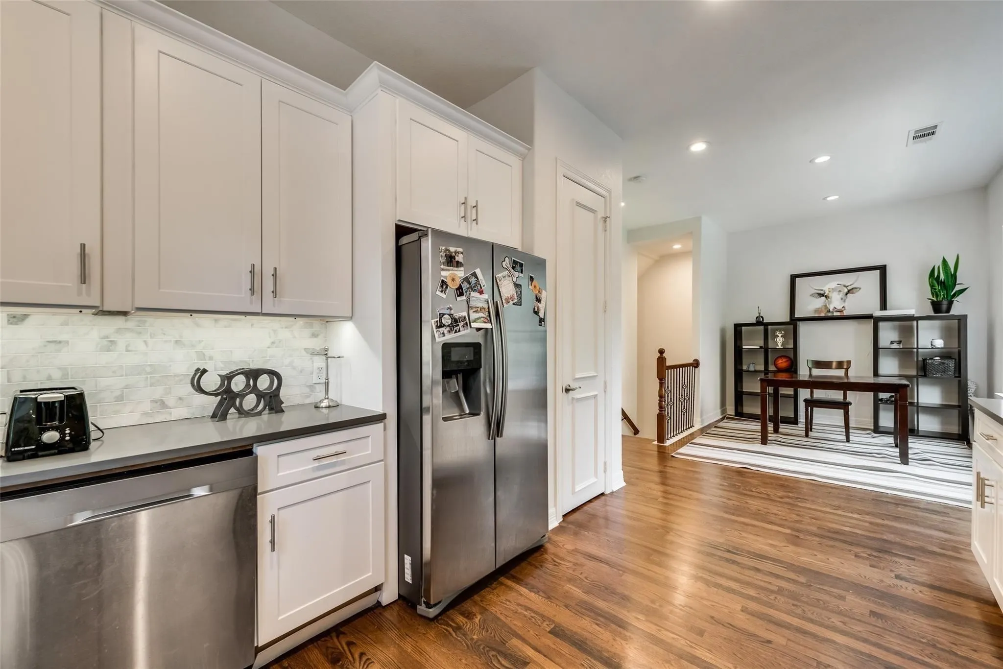 White shaker cabinetry, stainless steel appliances, dark wood-finish flooring, recessed lighting, and a white tile backsplash