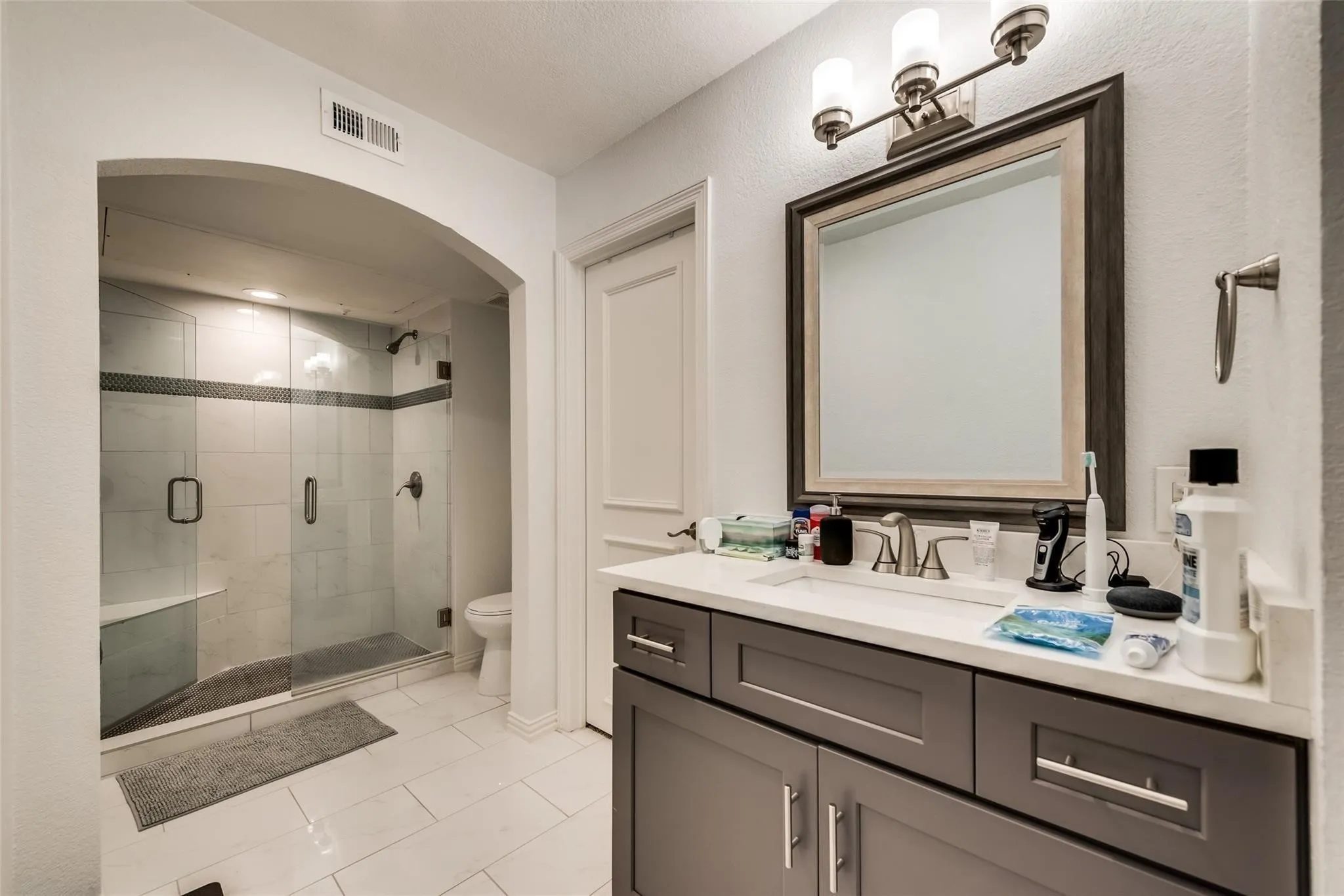 Vanity with a single basin sink, white countertop, and dark cabinetry