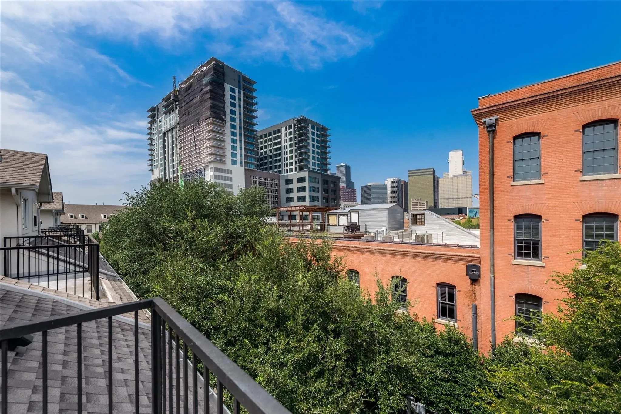 Rooftop balcony with black metal railing, gray shingle roofing, and lush trees