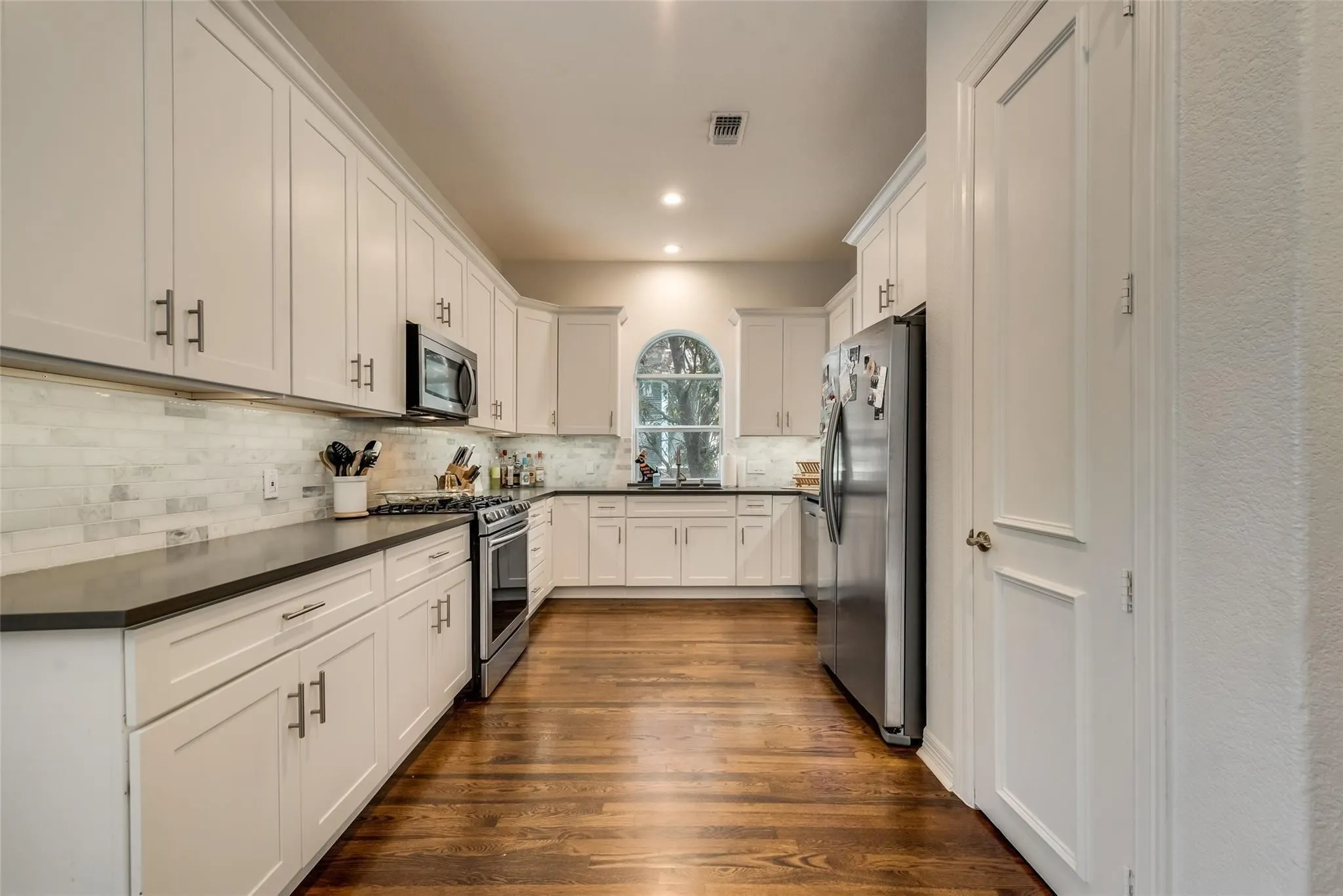Well-appointed kitchen featuring extensive white cabinetry, dark countertops, a subway tile backsplash, stainless steel appliances, and wood-finish flooring