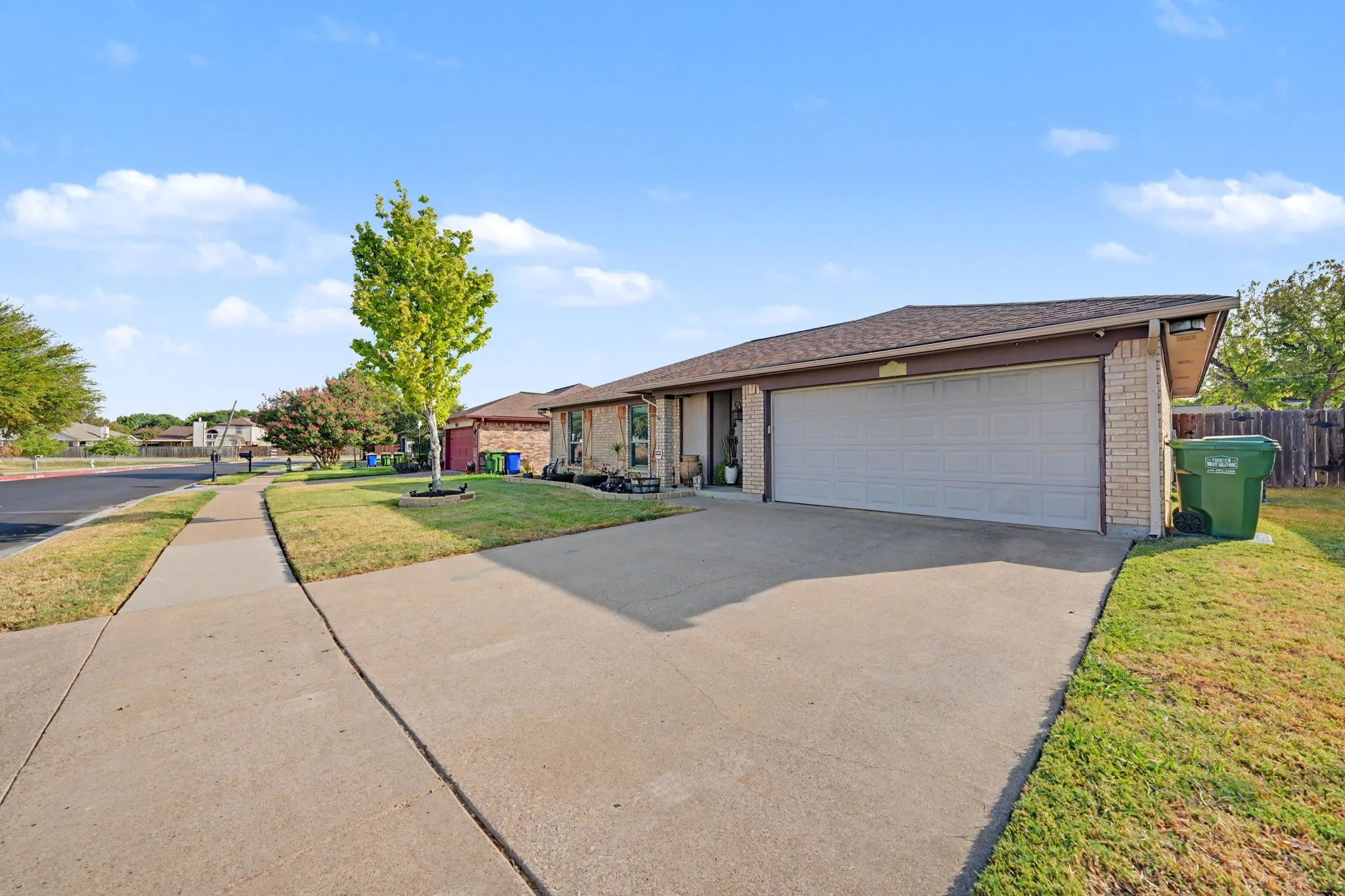 Brick exterior with an attached two-car garage, concrete driveway, and mature landscaping