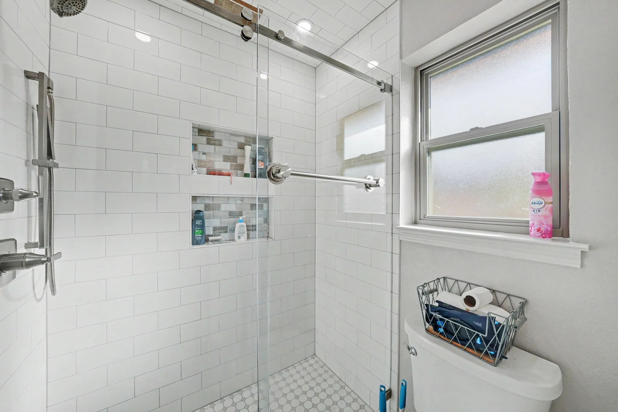 Shower enclosure with subway tile surround, clear glass door, dual recessed shelving, and a hexagon tile floor