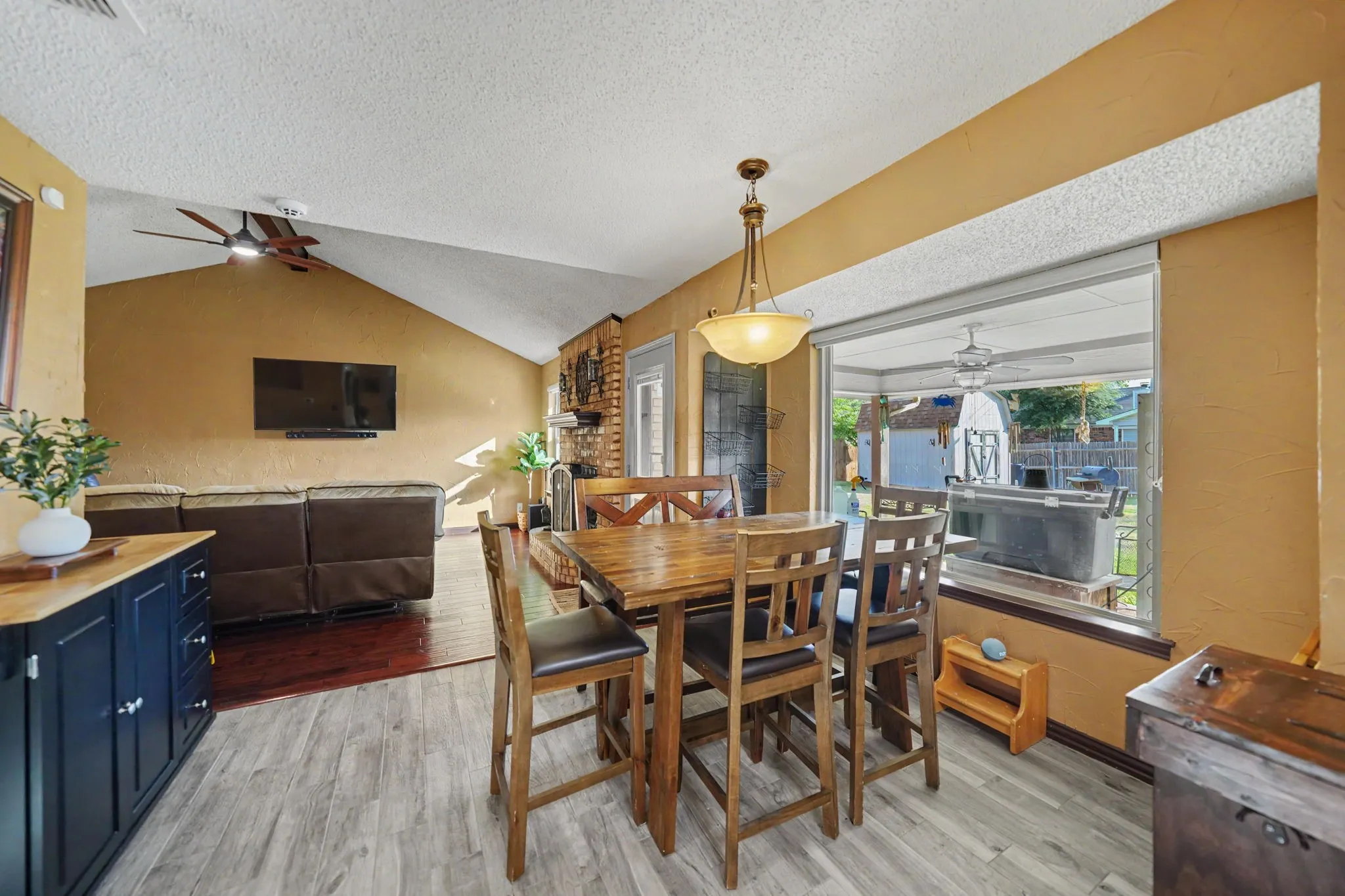 Vaulted ceilings, wood-finish flooring, brick fireplace, built-in cabinetry, and a large pass-through window