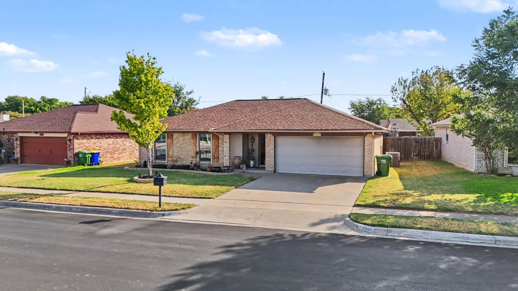 Brick facade residence featuring a two-car garage, mature front yard tree, and an asphalt shingle roof