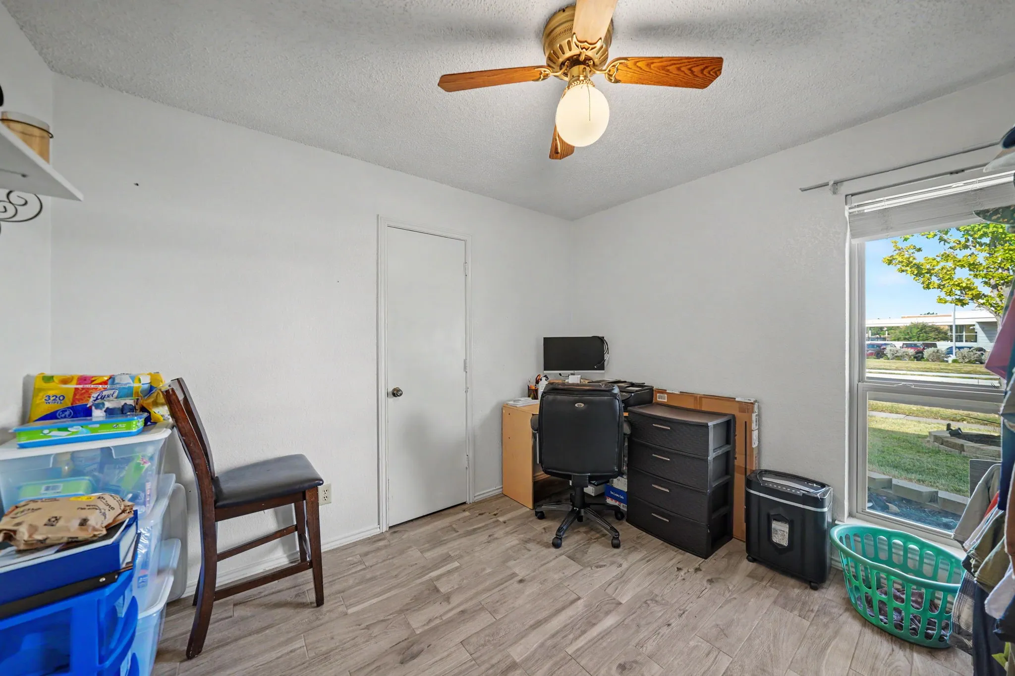 Versatile bedroom featuring wood-finish flooring, ceiling fan with integrated lighting, and abundant natural light from large windows overlooking outdoor grounds