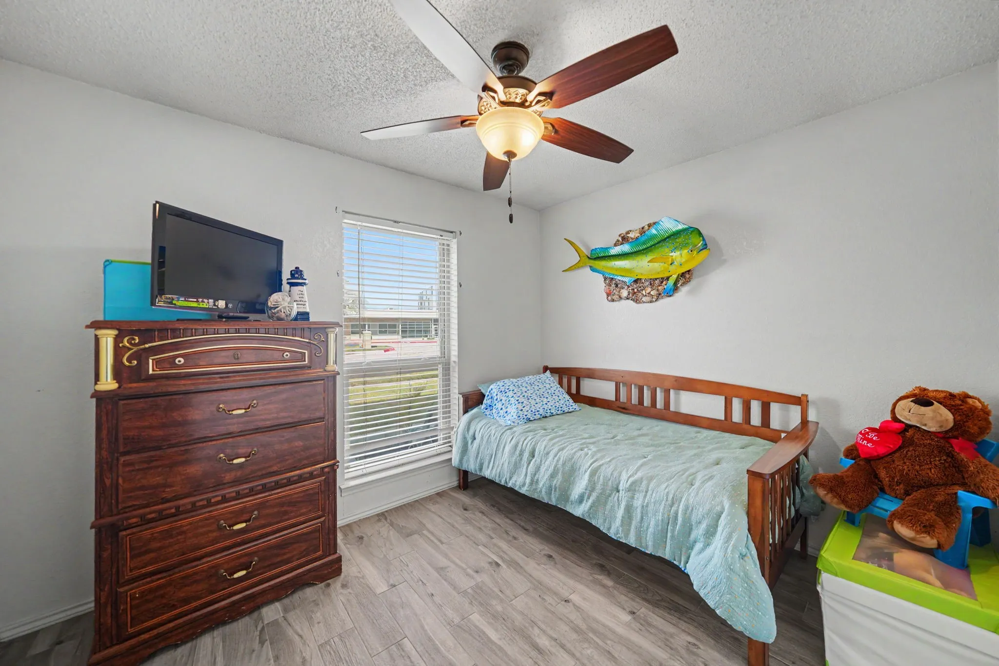 Wood-finish flooring with neutral wall paint, a window featuring horizontal blinds, and a ceiling fan with integrated lighting