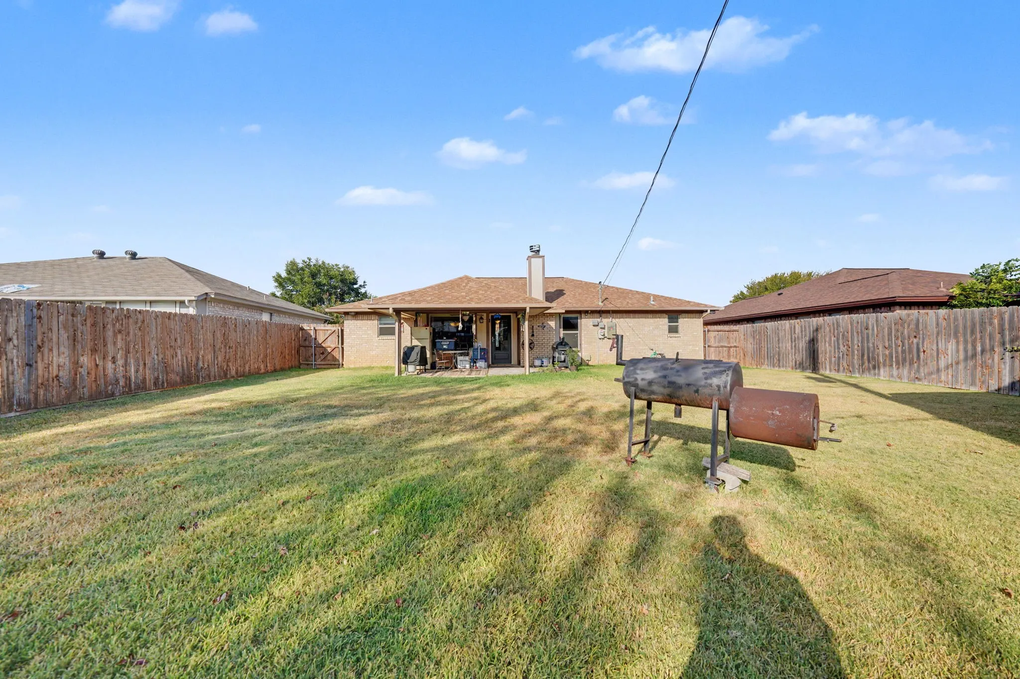 Expansive backyard featuring a large grass area, wood privacy fencing, and a covered patio with a concrete slab