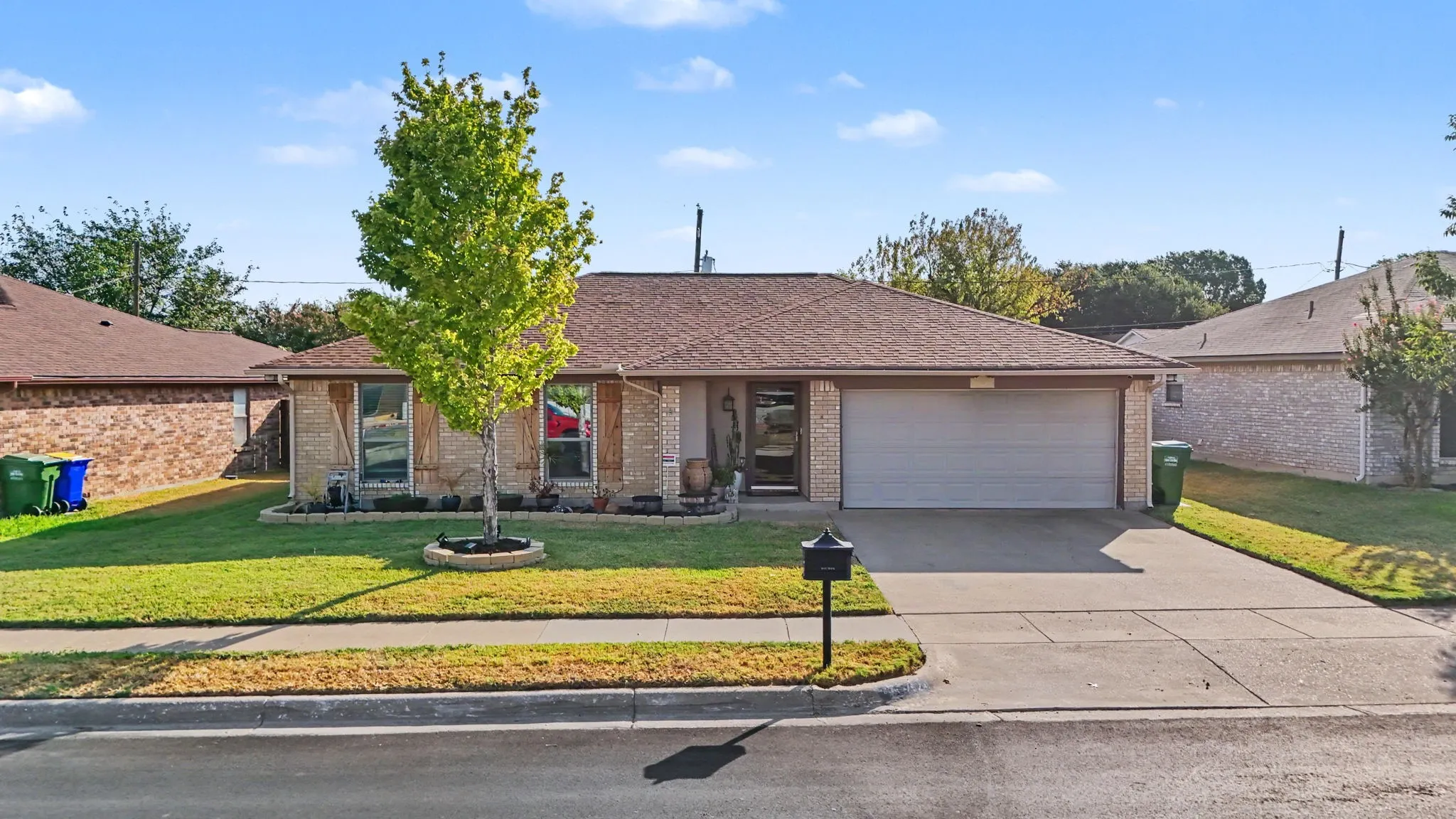 Brick exterior with an attached two-car garage, concrete driveway, and front lawn with a single tree