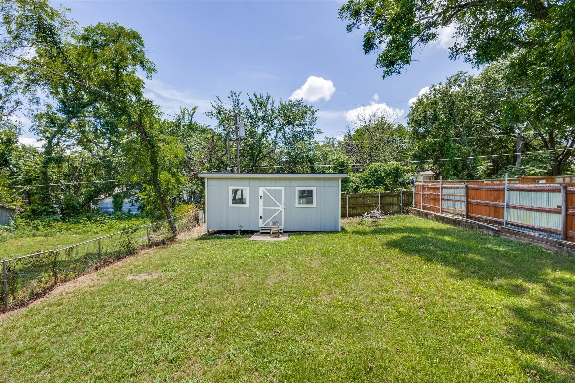 Expansive grassy yard with a storage shed featuring a single door and two windows