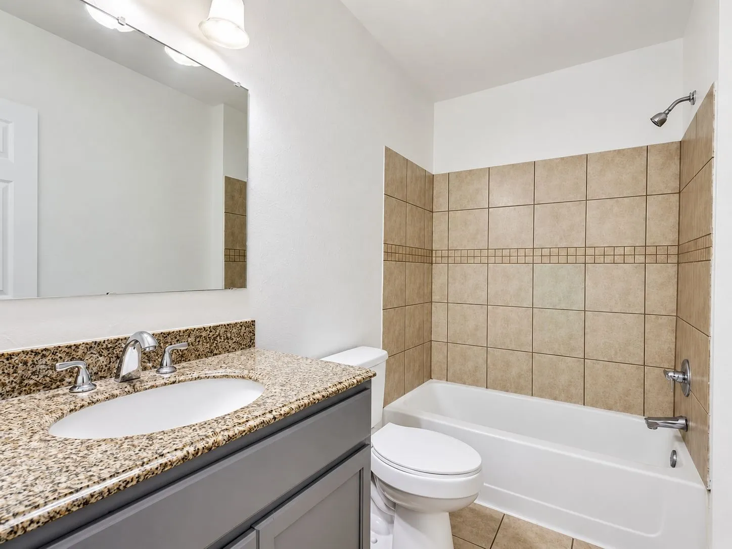 Bathroom featuring a vanity with a granite countertop, undermount sink, tiled bath surround, and ceramic tile flooring