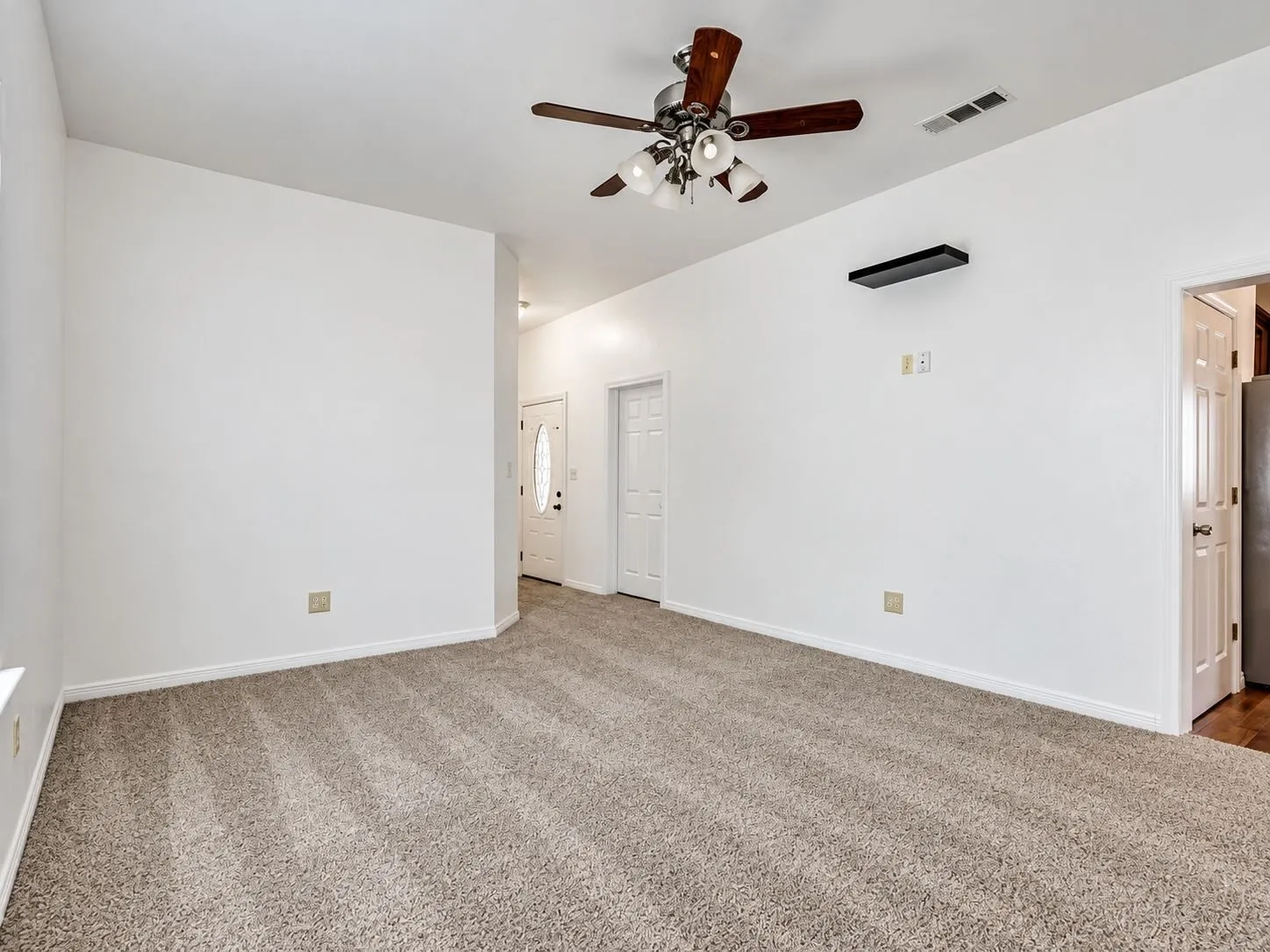 Carpeted room with white walls, ceiling fan with light, and a white paneled door