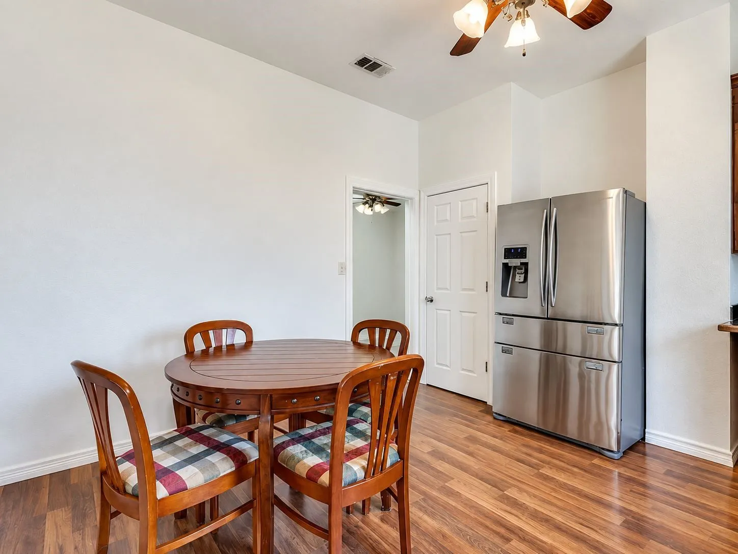 Wood-finish flooring with a stainless steel refrigerator, white paneled door, and a ceiling fan with integrated lighting