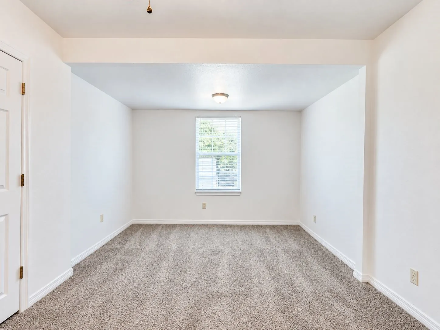 Recessed room with neutral carpeting, white walls, a single window with blinds, and an overhead flush-mount light fixture