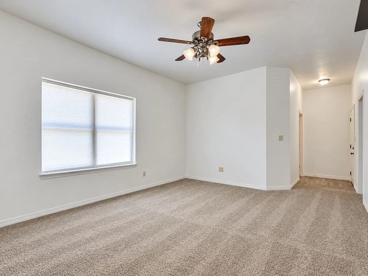 Spacious room featuring neutral carpeting, a large window with blinds, and a ceiling fan with integrated lighting
