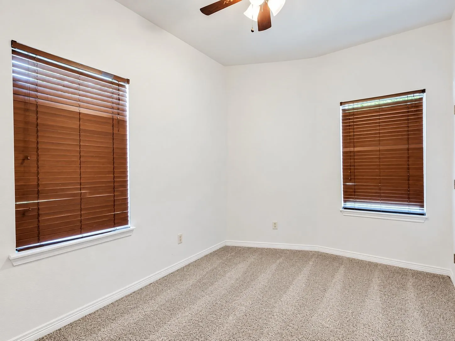 Vaulted ceiling room with two windows, wood-finish blinds, and textured carpet flooring