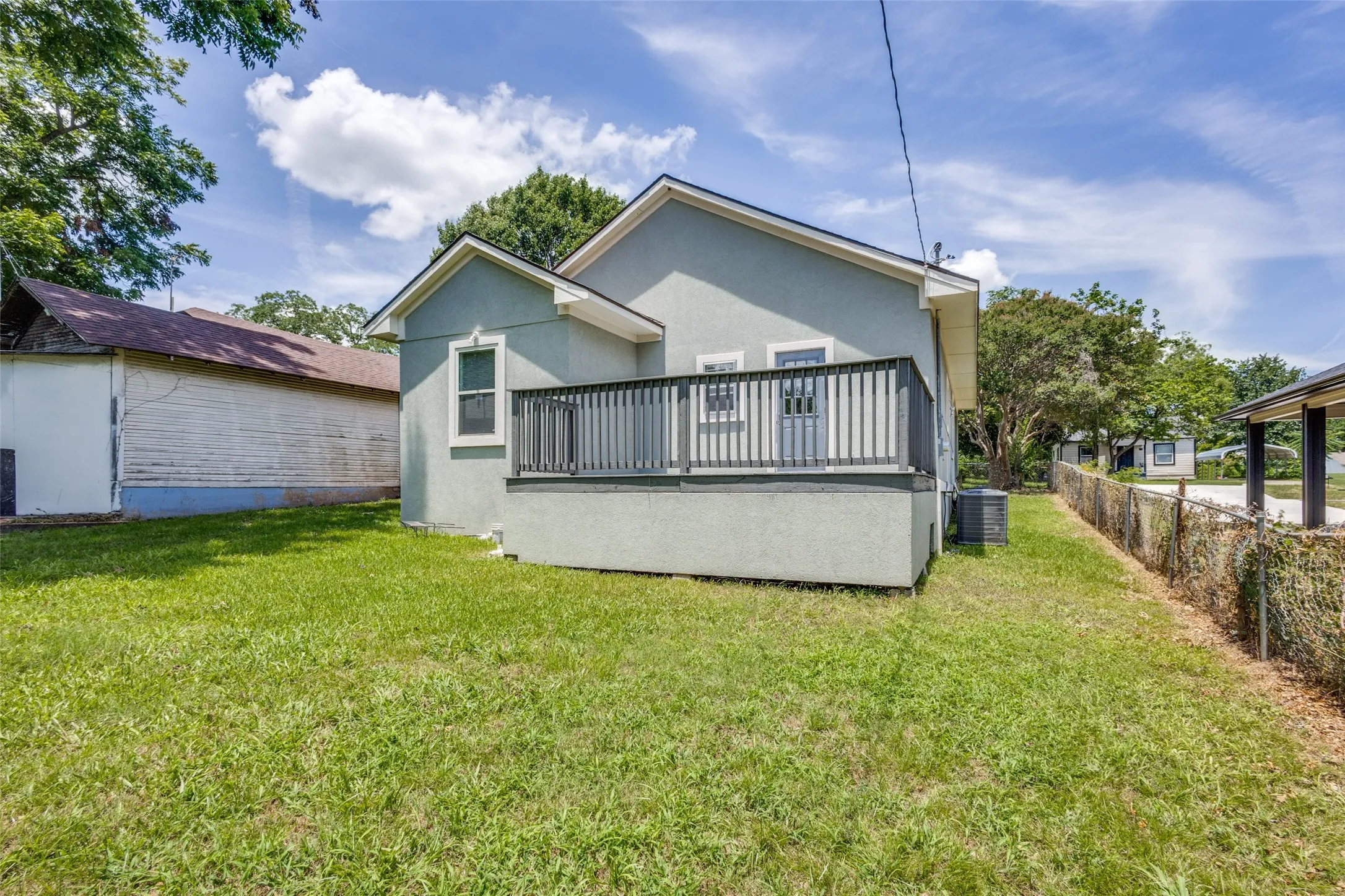 Rear exterior featuring a raised deck with dark railings, stucco siding, and a grassy yard