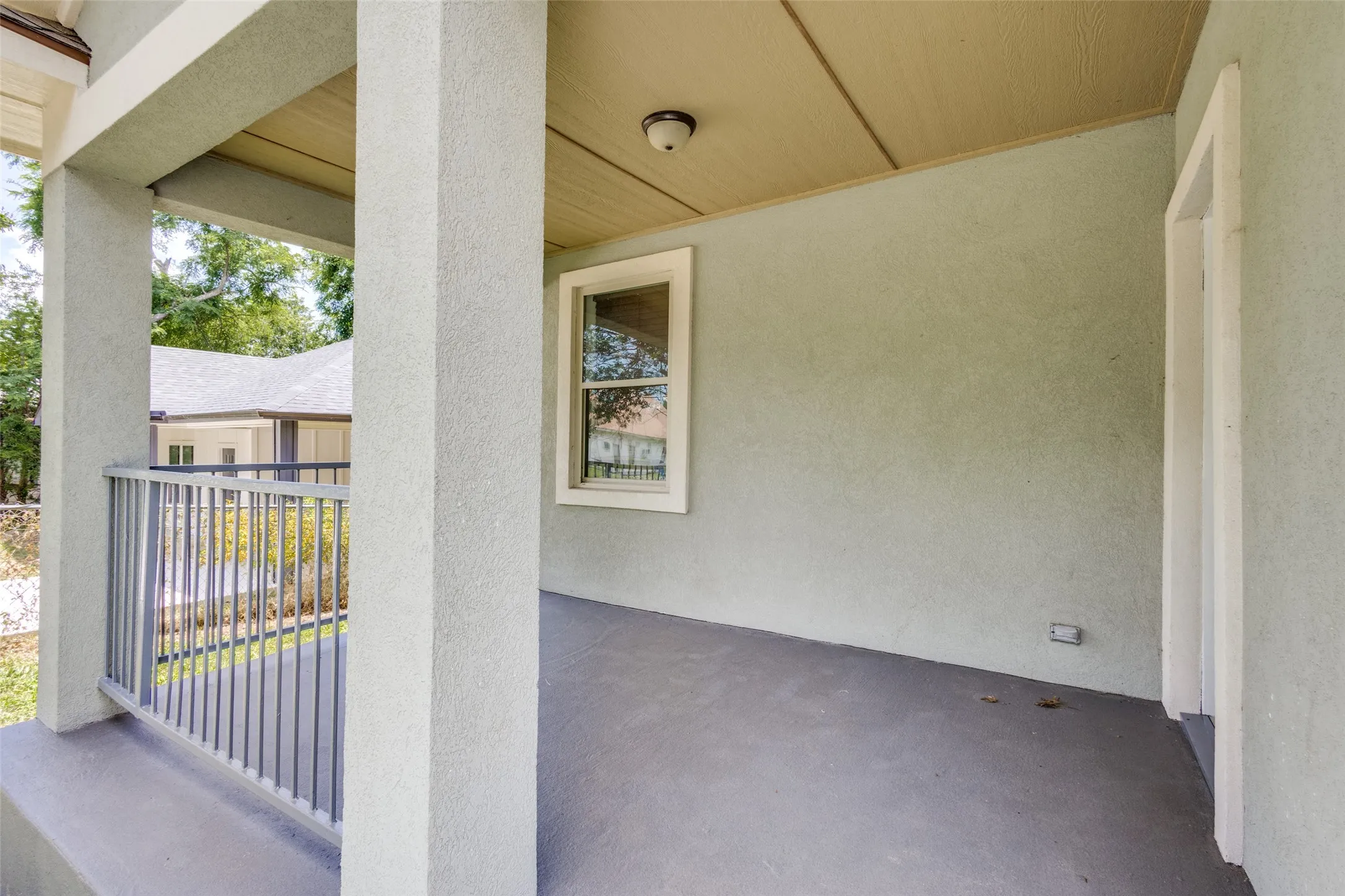 Covered porch featuring stucco columns, a painted concrete floor, and a metal railing