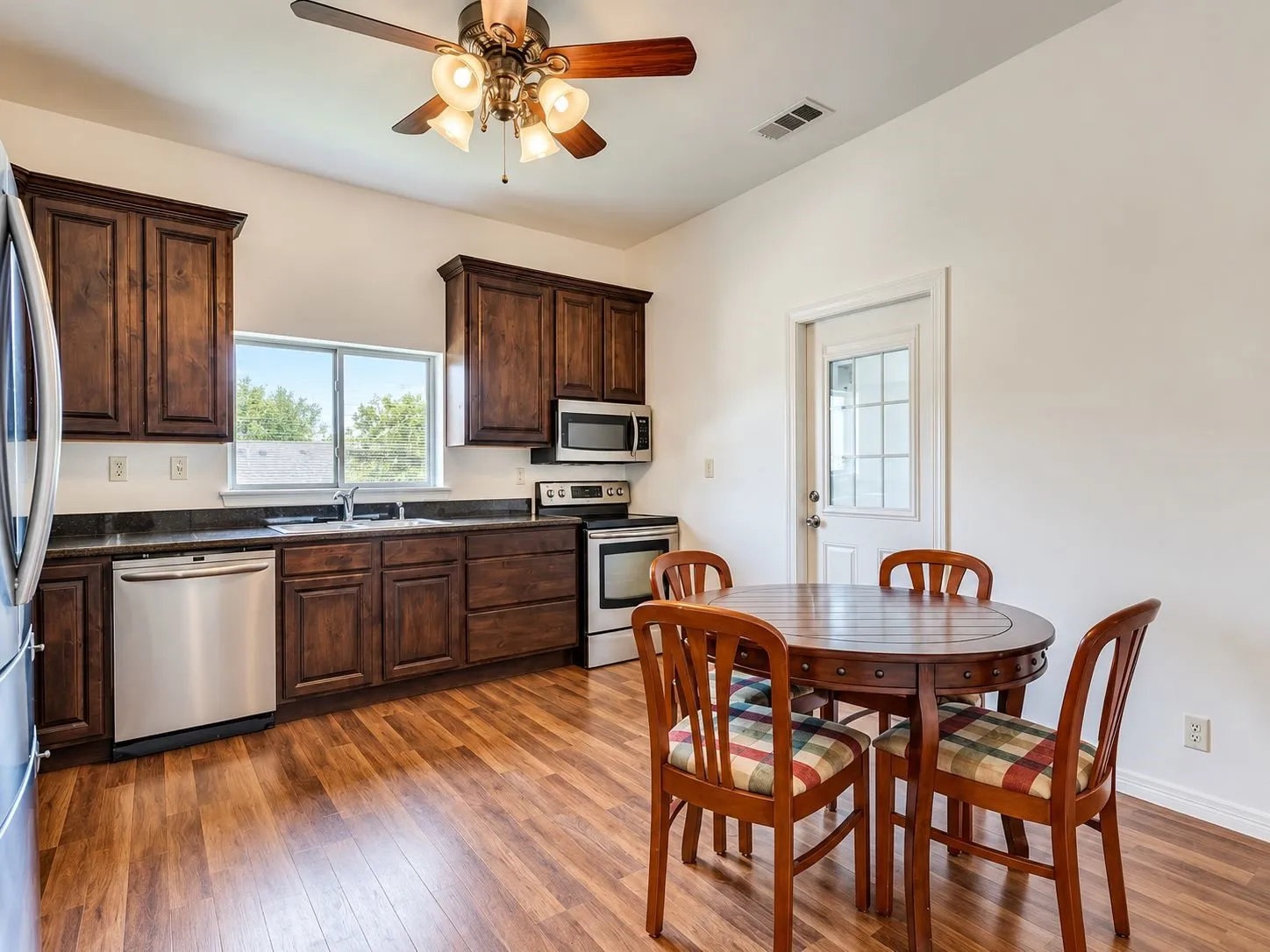 Kitchen featuring wood-finish flooring, dark wood cabinetry, stainless steel appliances, and a ceiling fan with integrated lighting