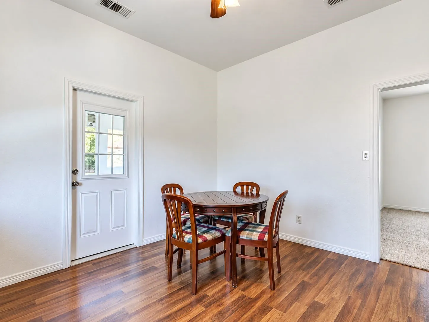Wood-finish flooring, white paneled door with window pane, white walls, and a ceiling fan