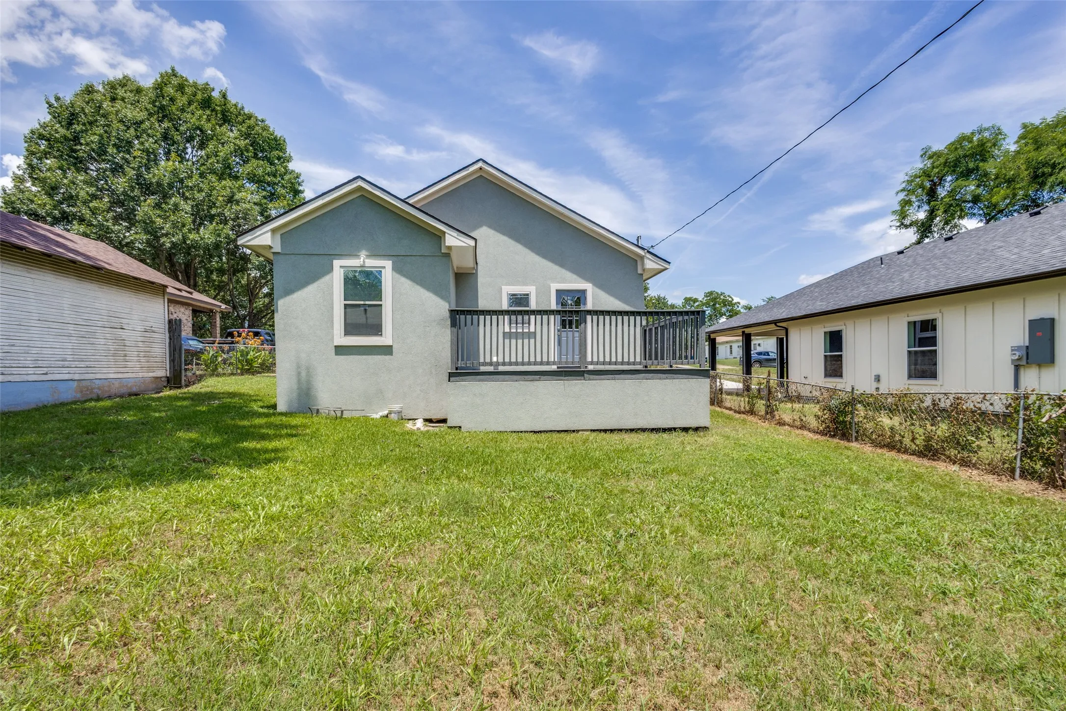 Expansive lawn with a raised deck, gray exterior siding, and a gabled roofline