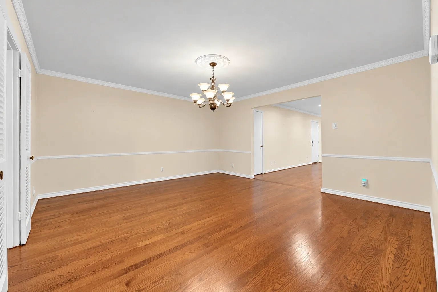 Hardwood flooring, decorative chandelier, crown molding, chair rail molding, and a spacious room layout