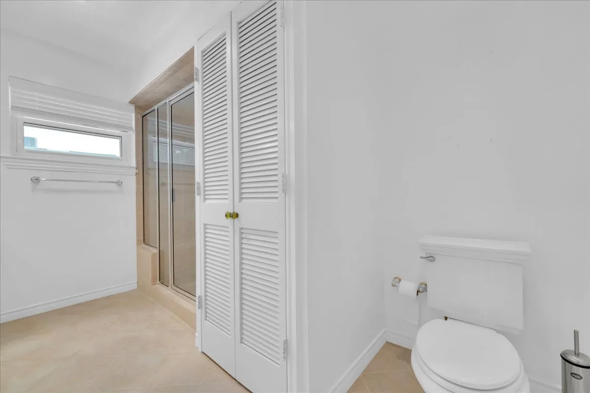 Recessed shower with glass enclosure, louvered bi-fold doors, window with privacy blind, and tiled flooring