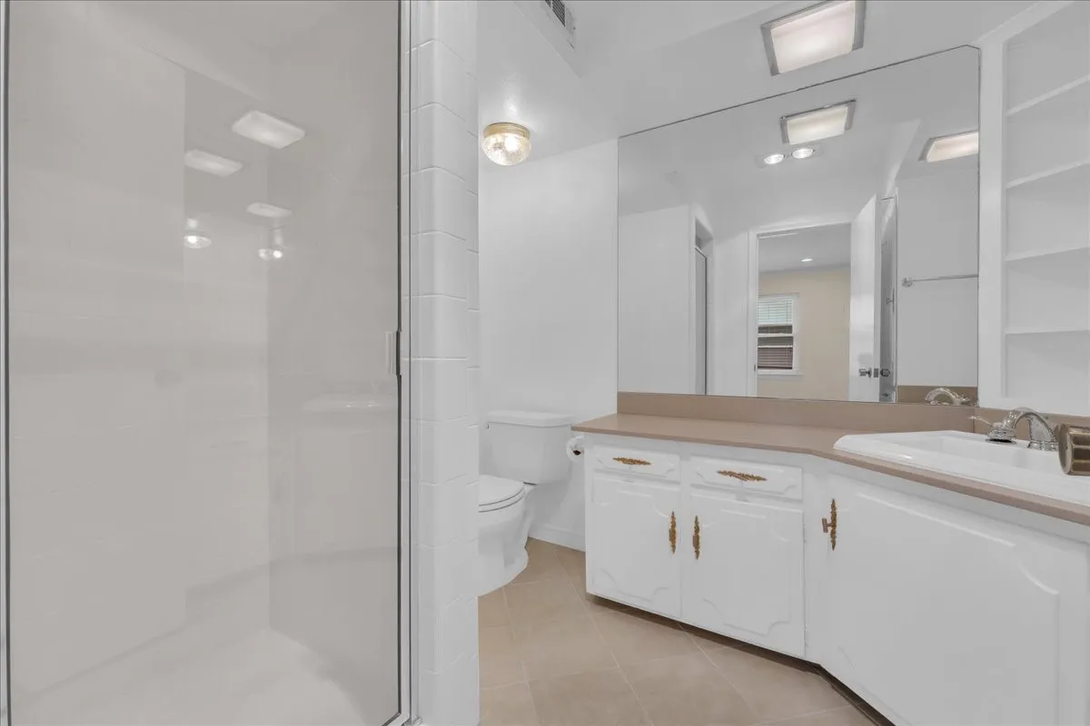 Glass-enclosed shower, built-in vanity with integrated sink, expansive wall mirror, built-in open shelving, and tiled flooring