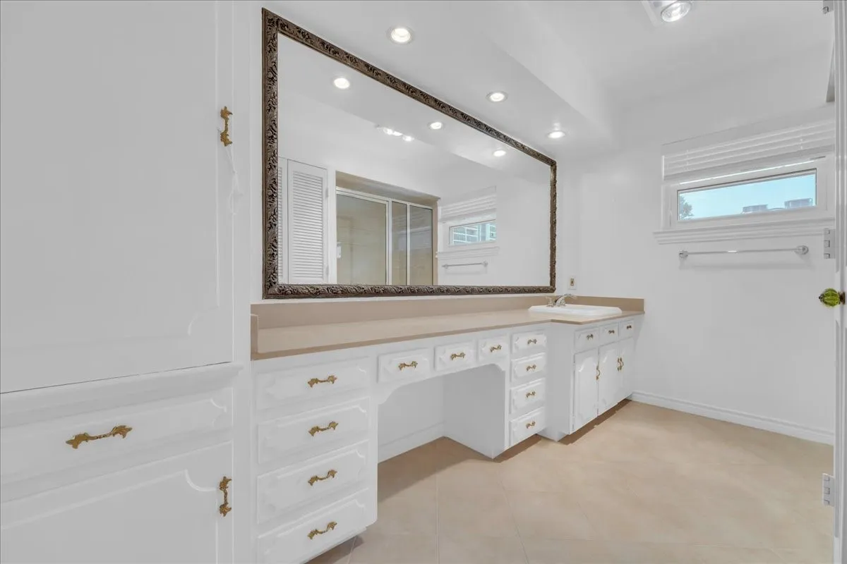 Integrated vanity with ample storage cabinetry, a drop-in sink, and an expansive wall-mounted mirror with an ornate frame