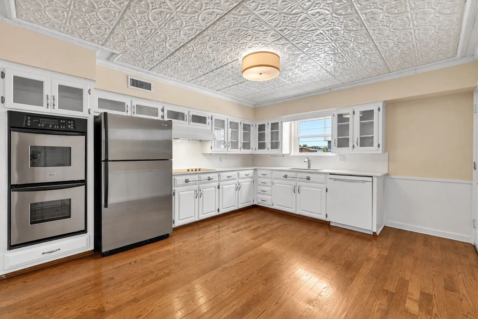Kitchen featuring wood-finish flooring, white cabinetry with glass-front uppers, stainless steel appliances, white countertops, and a decorative ceiling