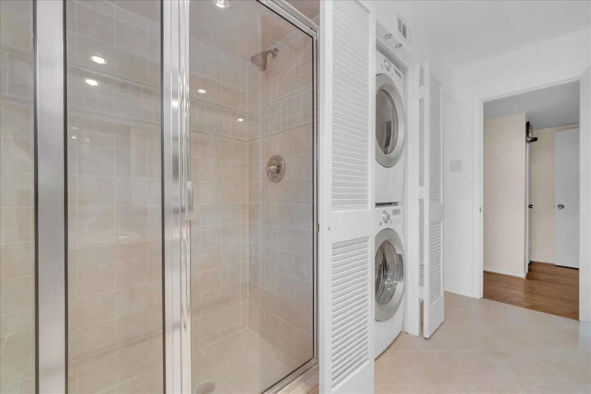 Glass-enclosed shower with tiled surround, chrome fixtures, and recessed lighting