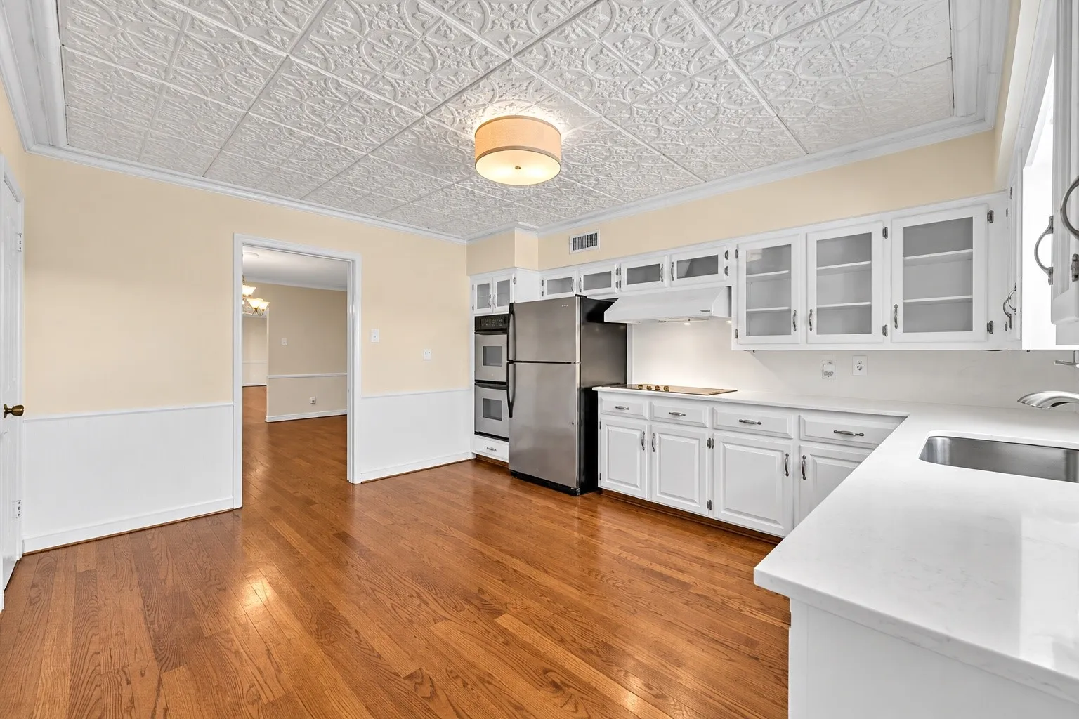 Kitchen featuring wood-finish flooring, white cabinetry with glass-front uppers, stainless steel double wall ovens, a stainless steel refrigerator, and light-toned countertops