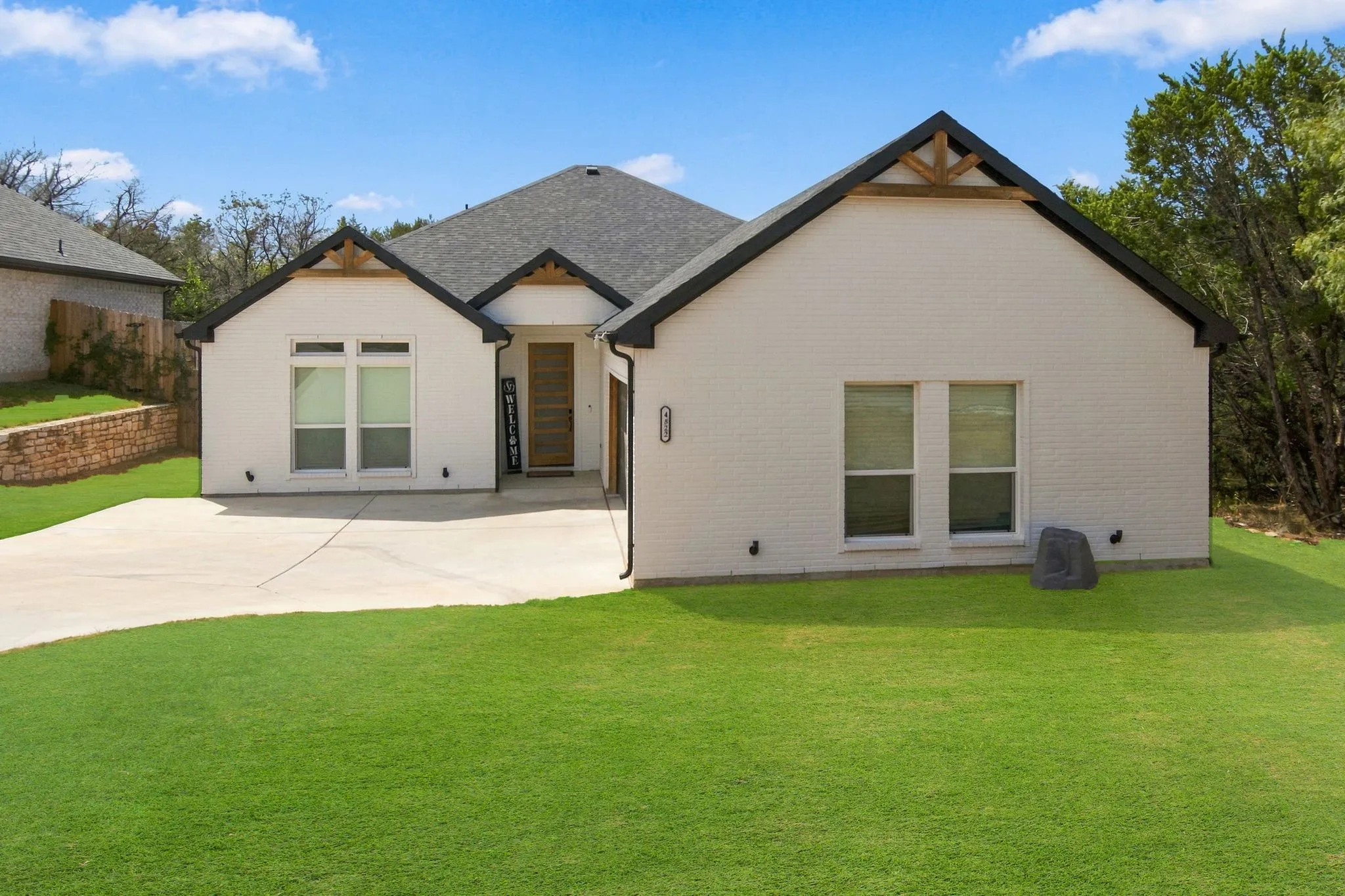 White brick exterior with dark trim, featuring a dark shingle roof and a concrete driveway