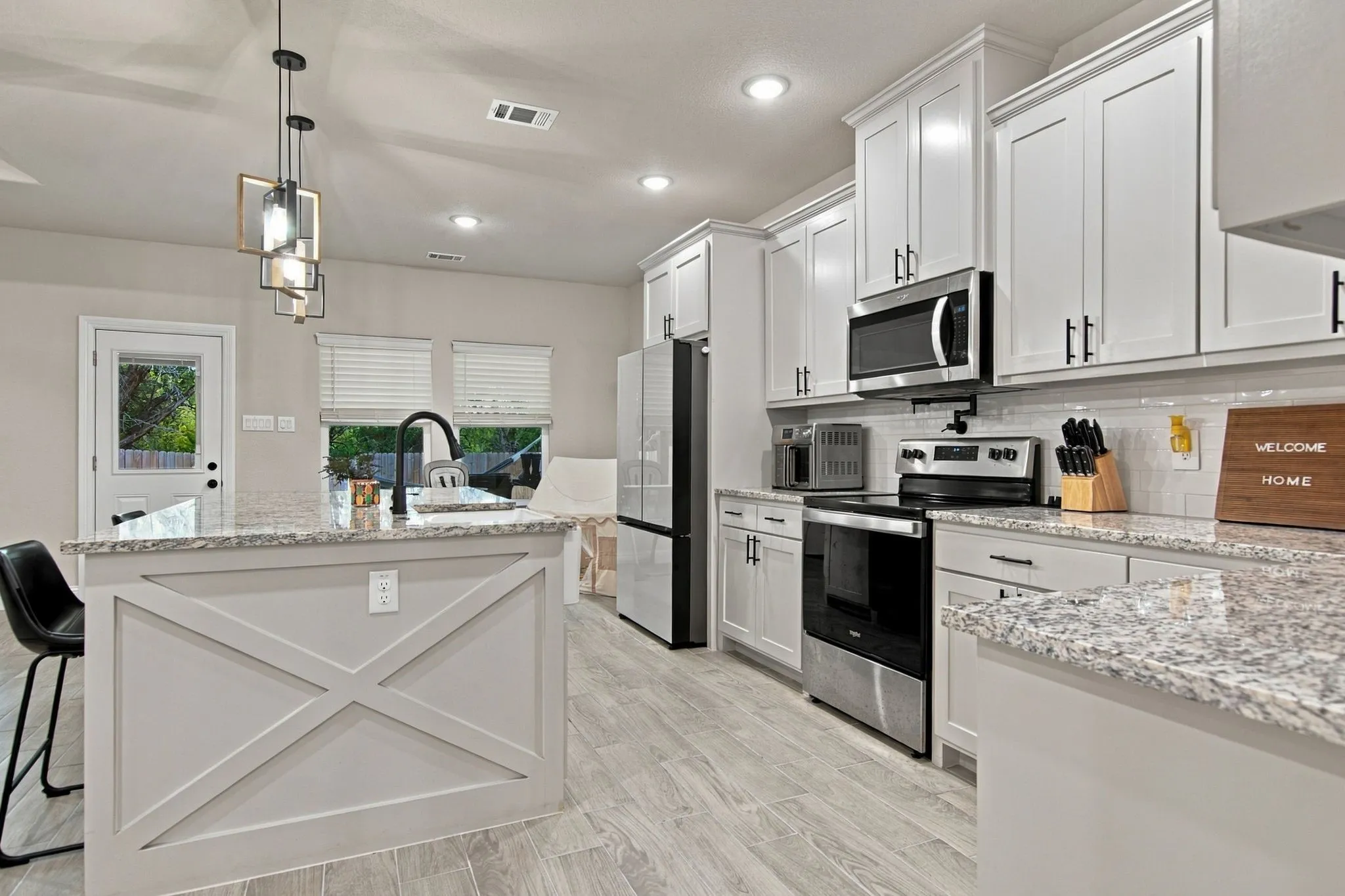 Kitchen featuring white shaker cabinetry, stainless steel appliances, light-toned granite countertops, and wood-finish flooring