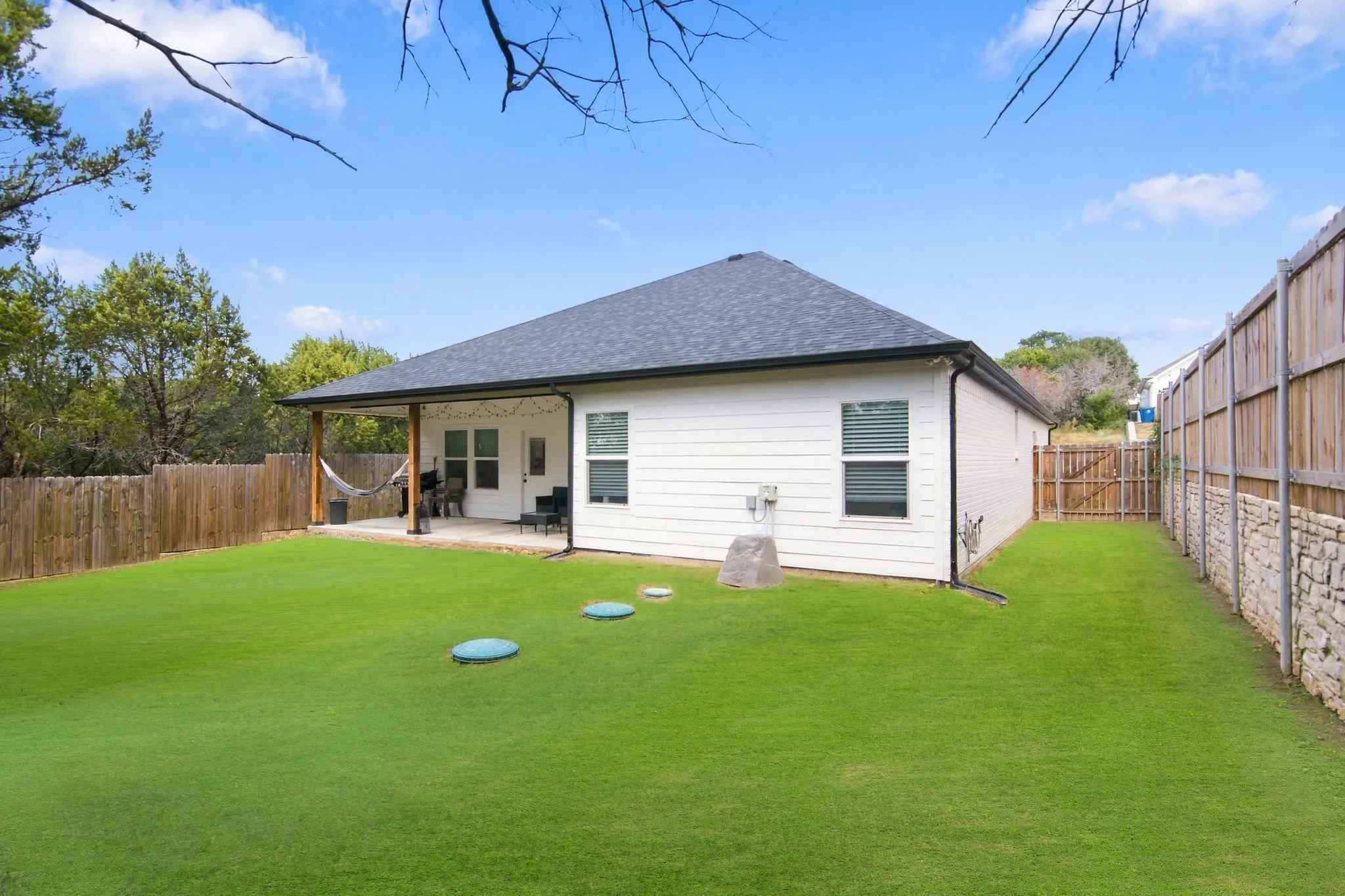 Expansive backyard featuring a covered patio with wood columns, a wood privacy fence, and a stone retaining wall