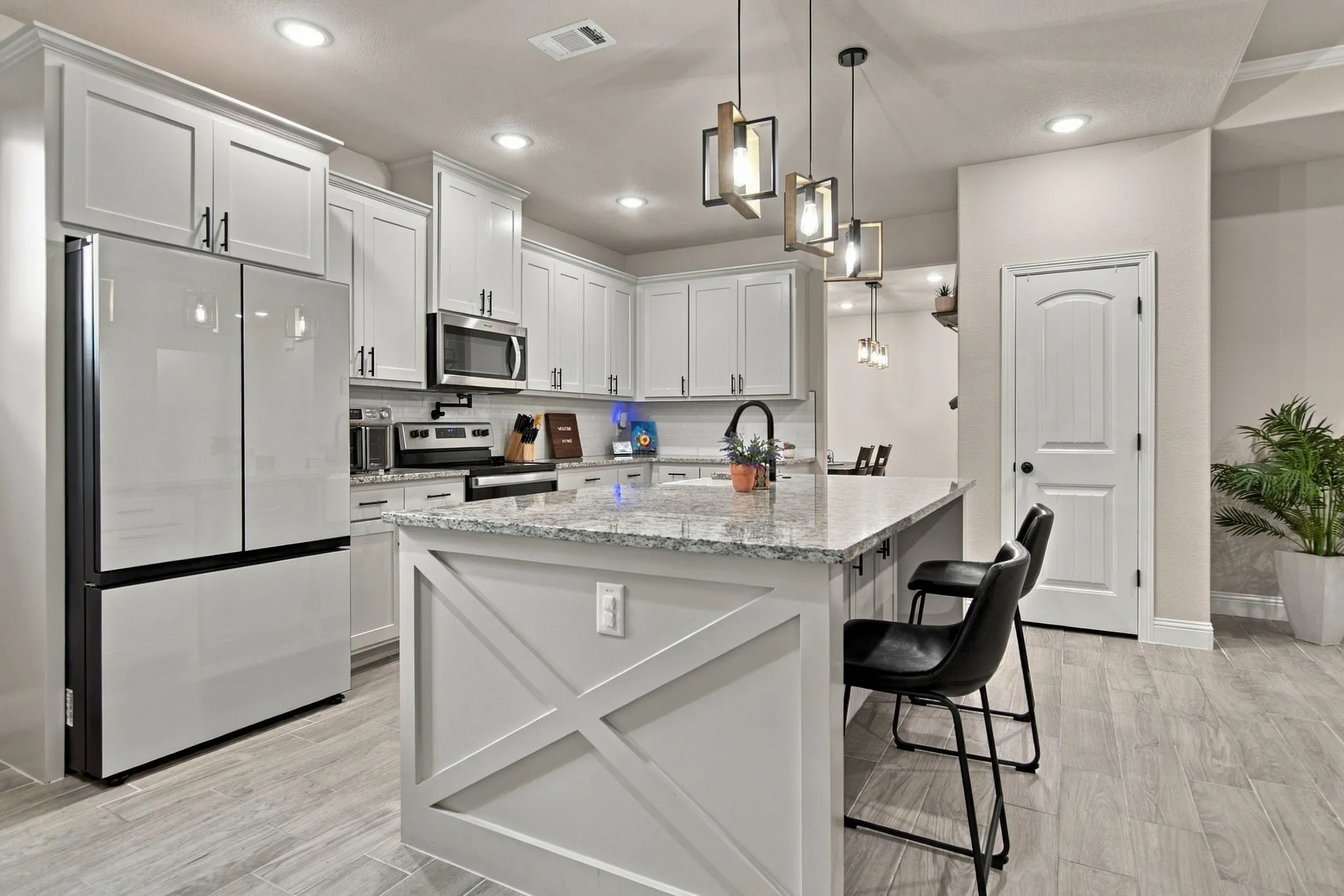 Kitchen featuring white shaker cabinetry, stainless steel appliances, a large island with decorative paneling, pendant lighting, and wood-finish flooring