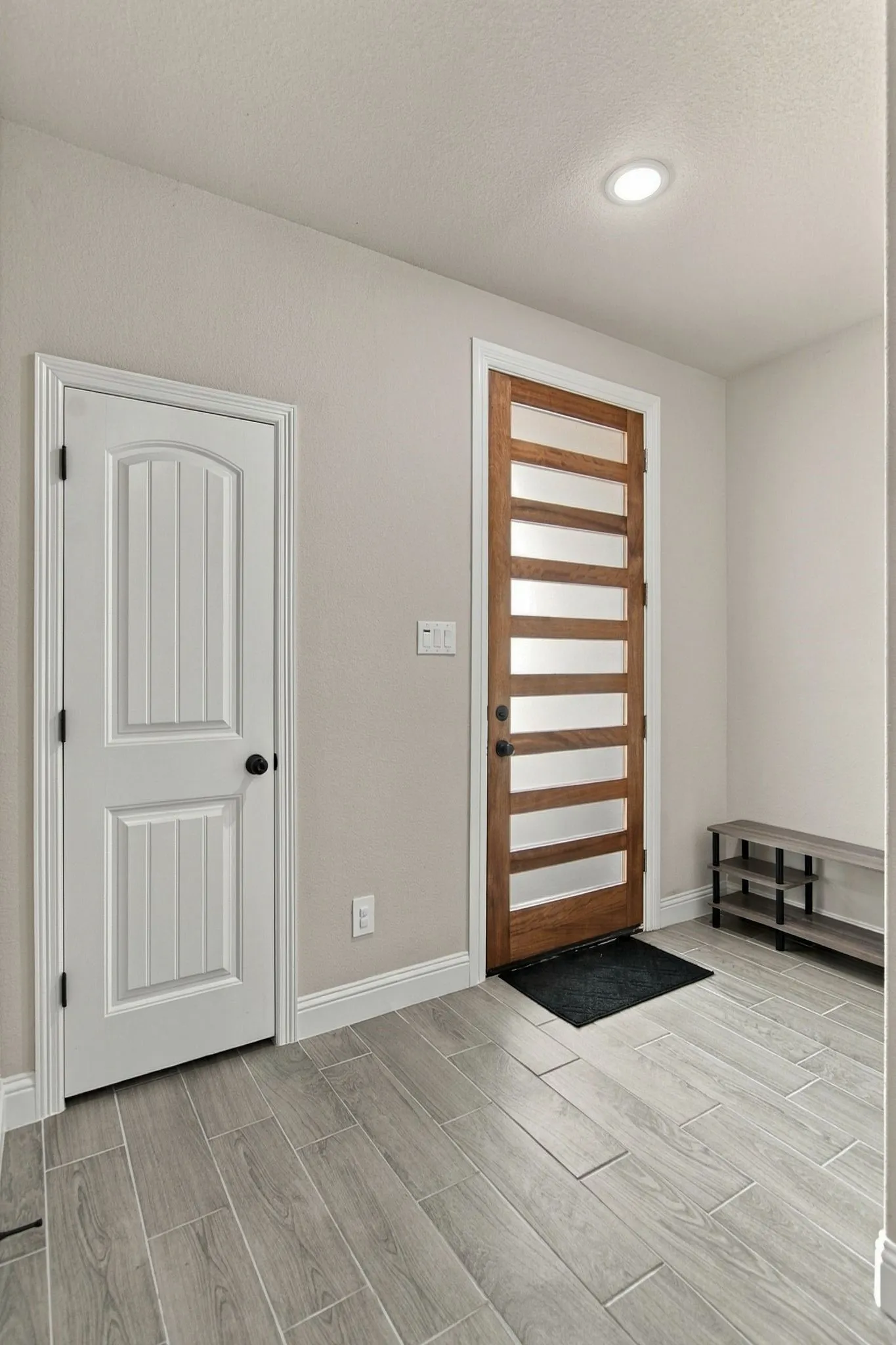 Entryway featuring wood-finish tile flooring, recessed ceiling lighting, and a modern wooden entry door with frosted glass panels
