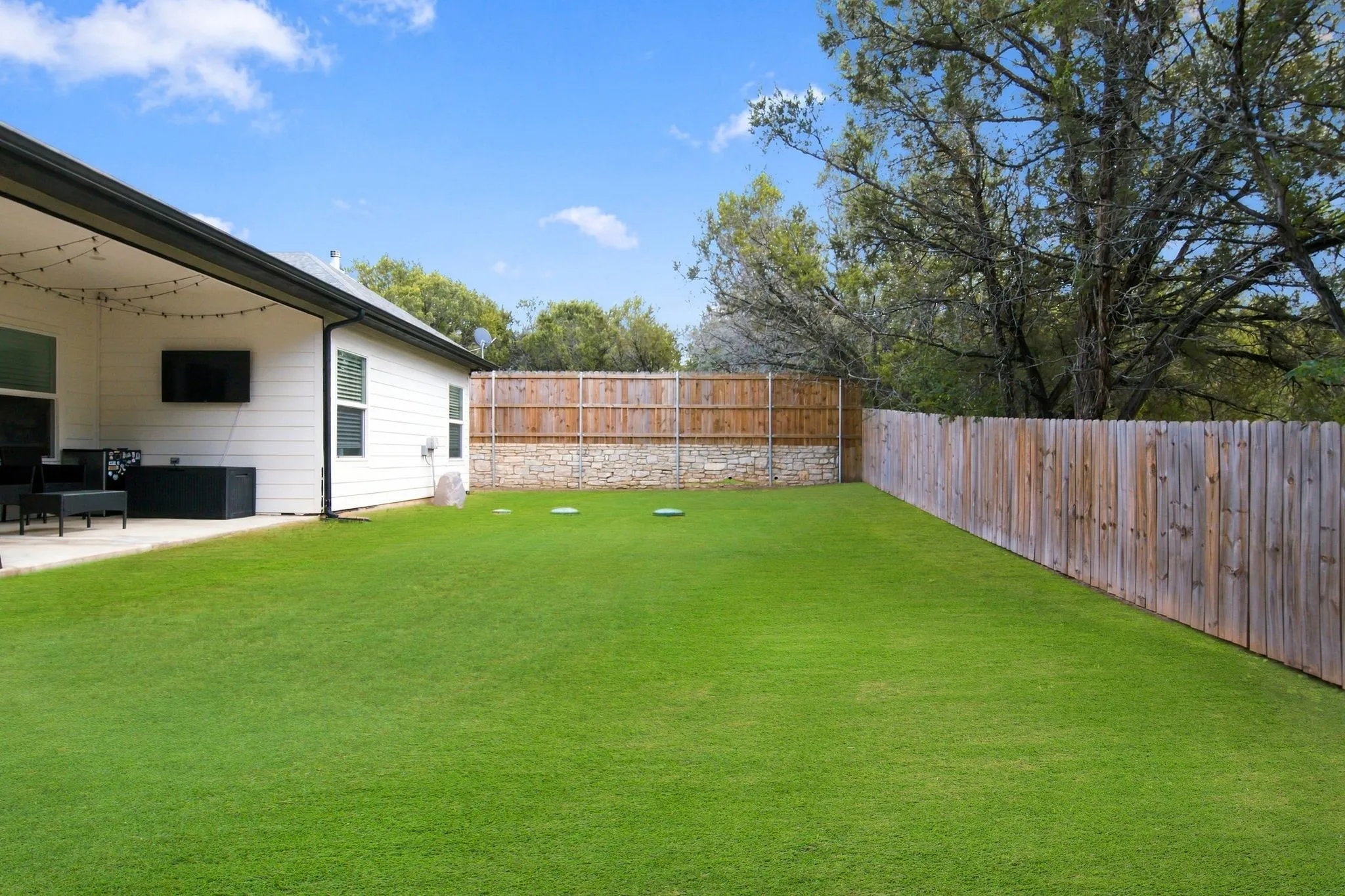 Expansive green lawn with a wood plank fence and a stone retaining wall
