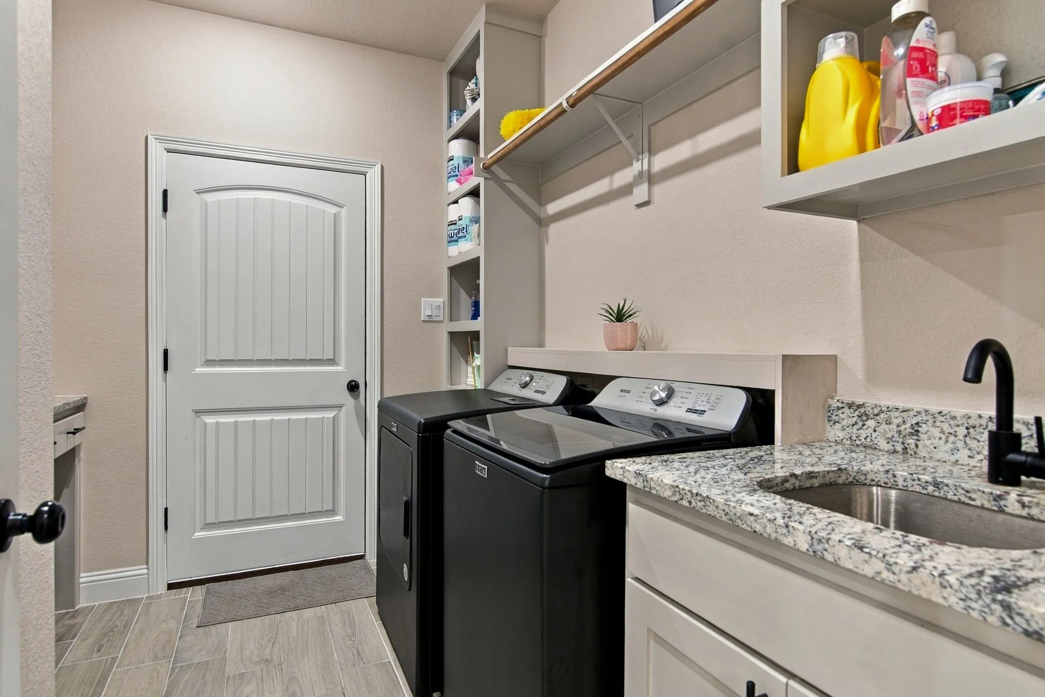 Utility room featuring a built-in sink with a matte black faucet, granite-style countertop, and ample storage with shelving and cabinets