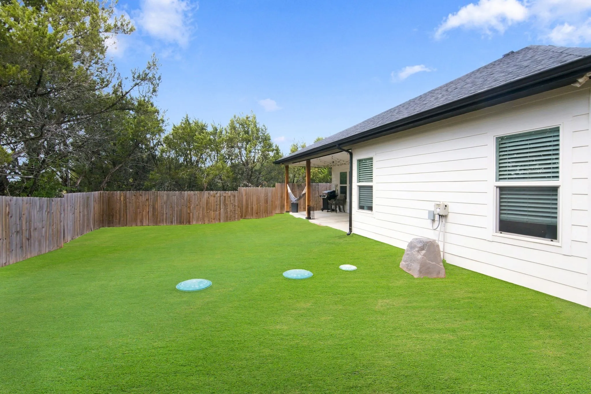 Spacious fenced backyard featuring a covered patio, broad lawn, and mature perimeter trees