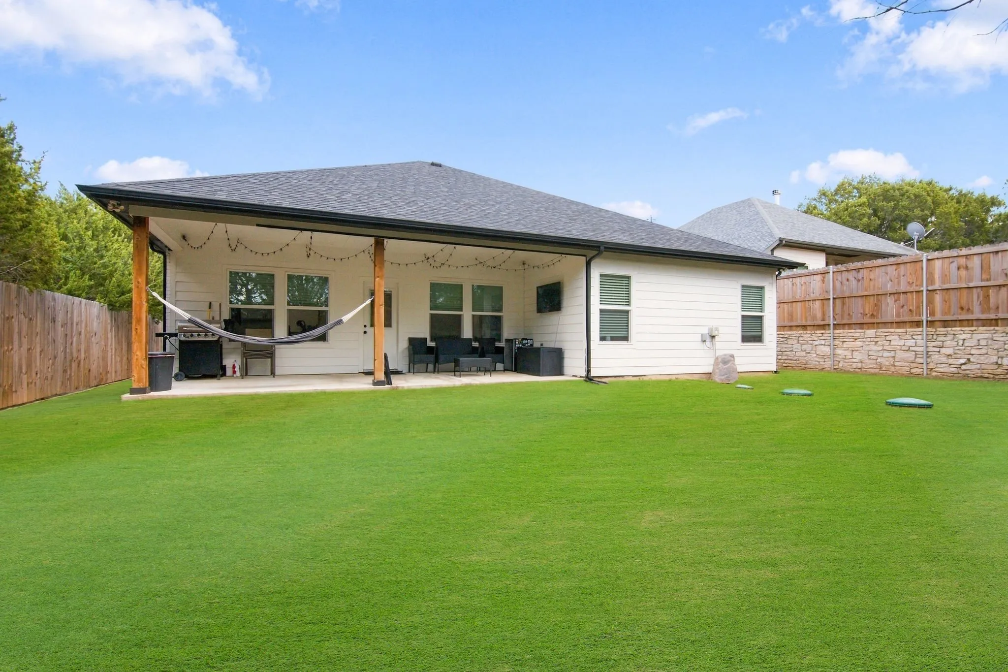 Expansive backyard with a covered patio, wood posts, and a white siding exterior
