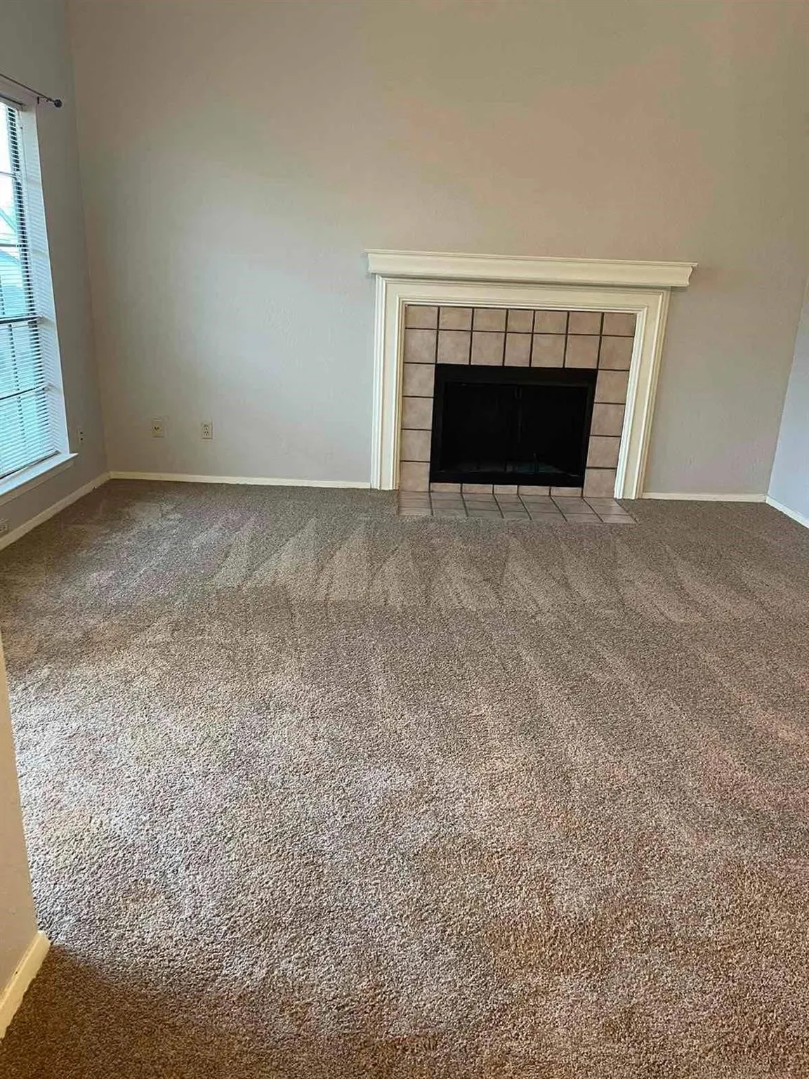 Carpeted living space featuring a fireplace with a tile surround and mantel, and a window with blinds