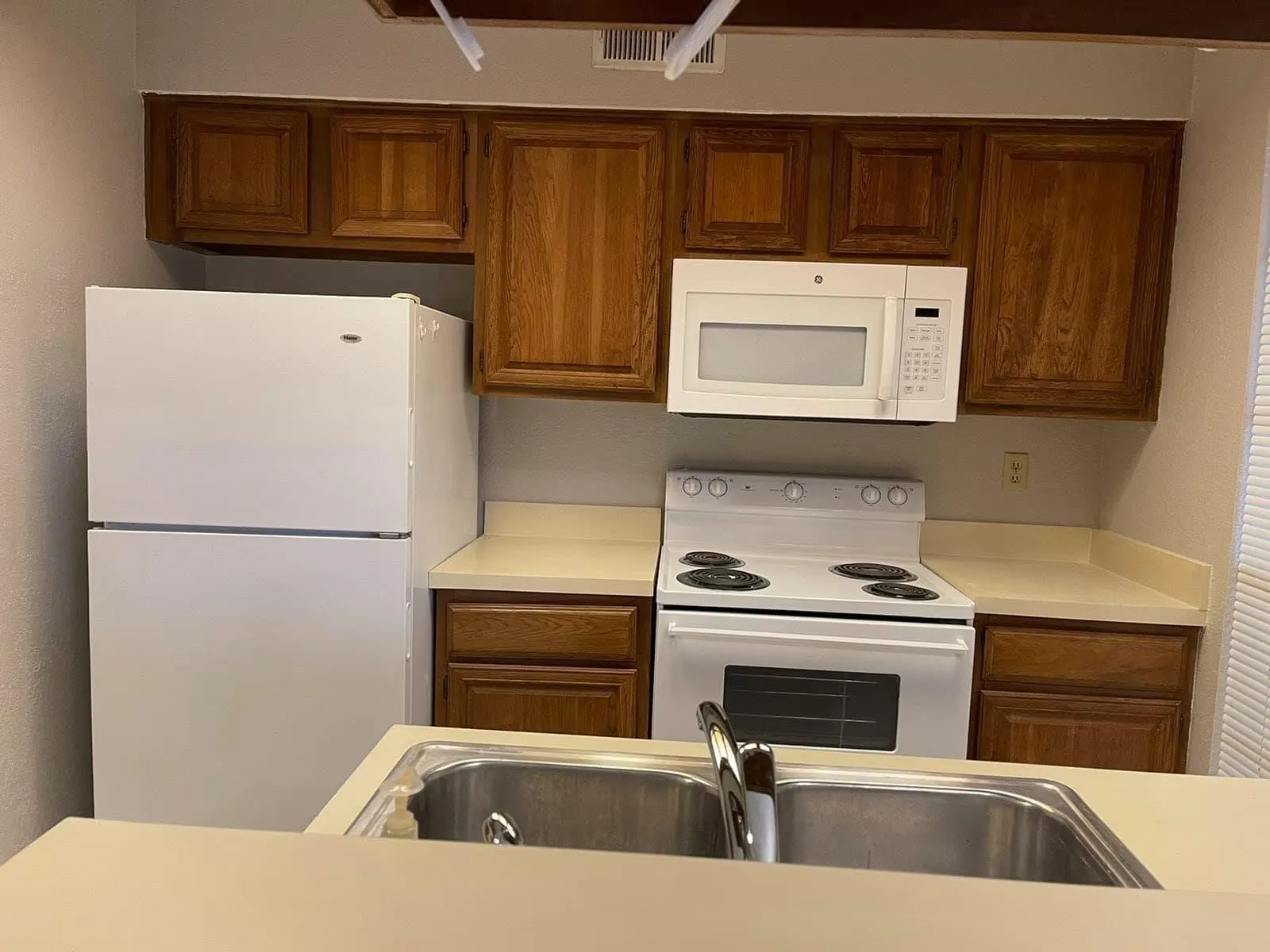 Kitchen featuring wood cabinetry, a stainless steel double basin sink, and white appliances including a refrigerator, range, and microwave