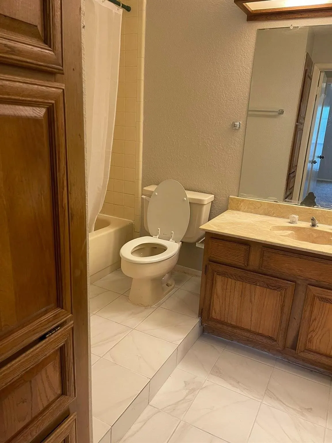 Bathroom featuring a tub/shower combination with tile surround, wood-finish vanity with countertop, and tile flooring