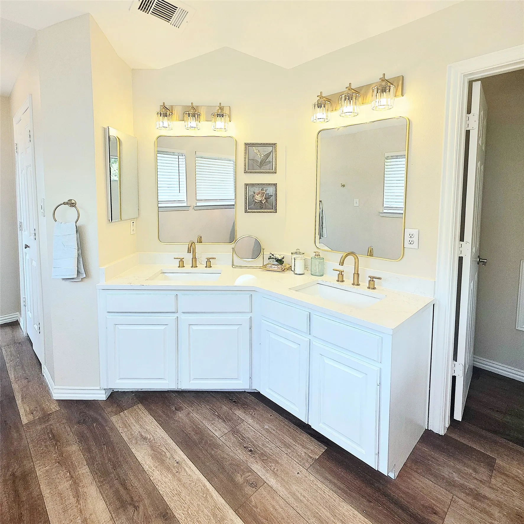 Getting ready for the day is a breeze in this updated Hollywood Glam suite complete with Dual vanity.  white cabinets, gold-finish fixtures, coordinating rectangular mirrors, and wood look luxury vinyl plank flooring