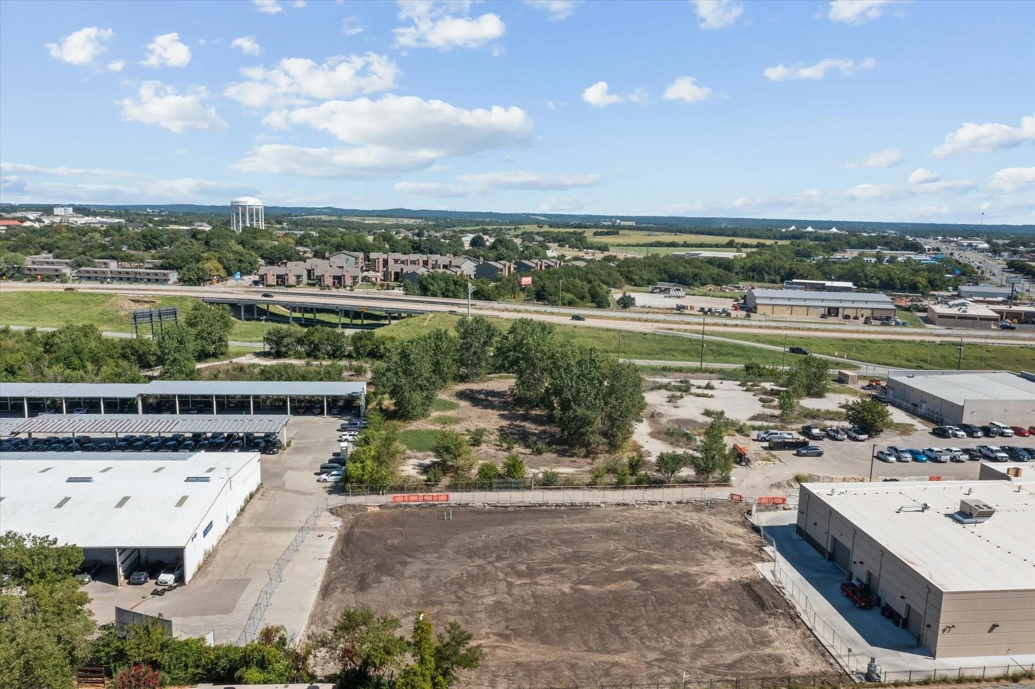 Expansive cleared lot with surrounding commercial structures and highway access