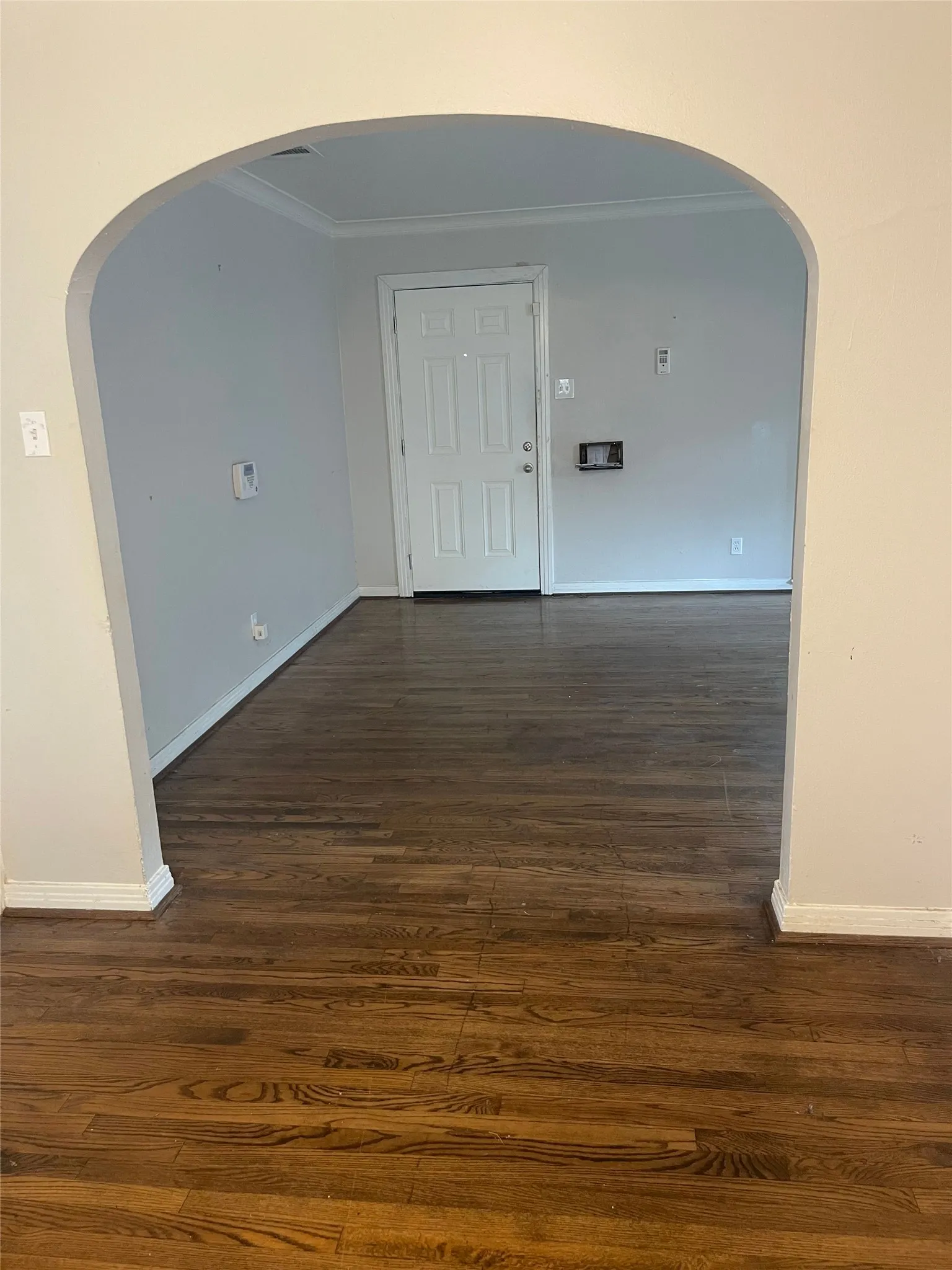 Archway entry with wood-finish flooring, crown molding, and a paneled entry door