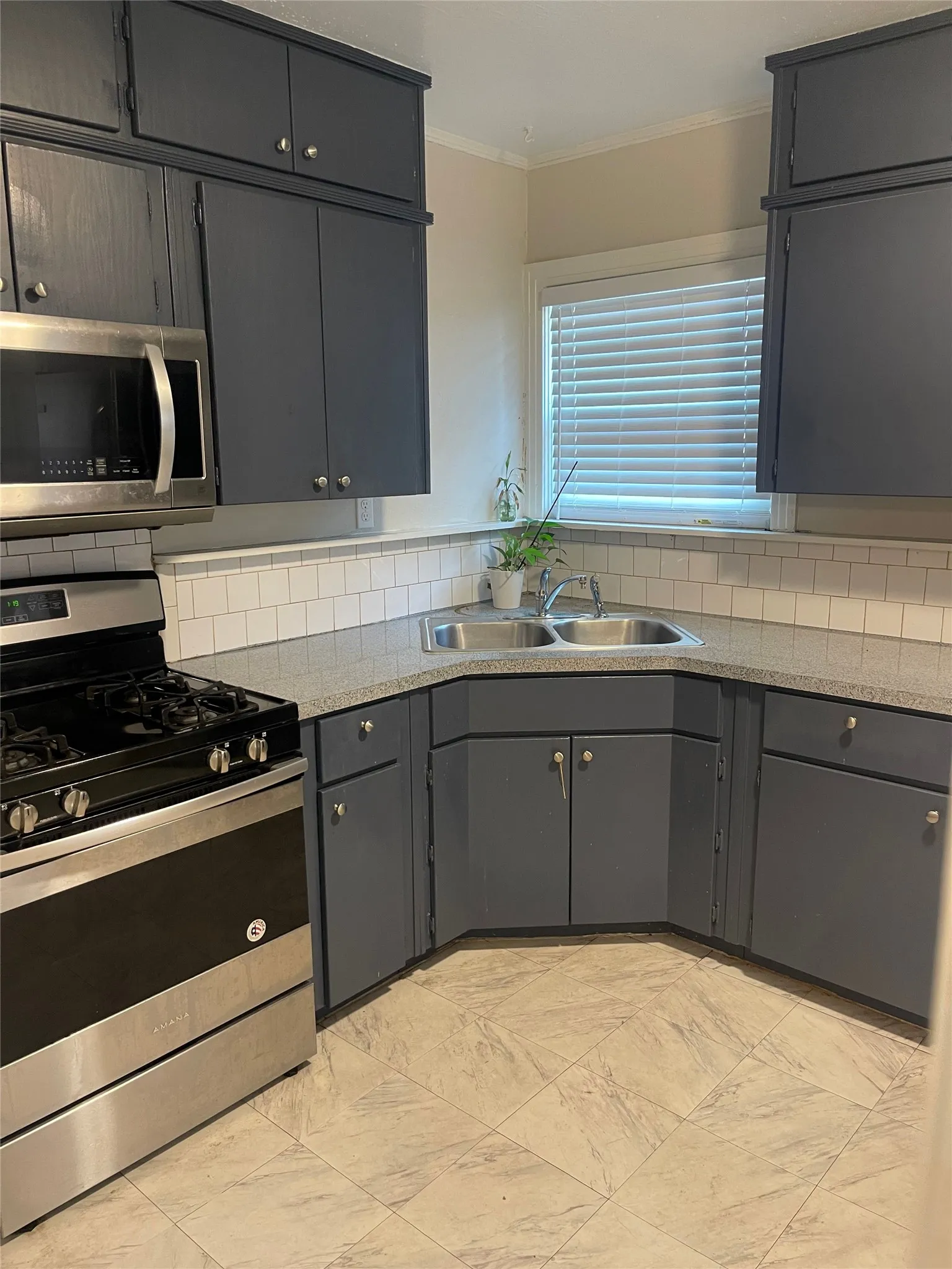 Stainless steel range with matching microwave, gray cabinetry, textured countertops, subway tile backsplash, and light-toned tile flooring